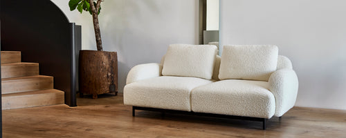 Hyggelig, moderne topersoners sofa med bløde puder på en slank metalramme, ledsaget af en stilfuld plantekasse og minimalistisk dekoration.