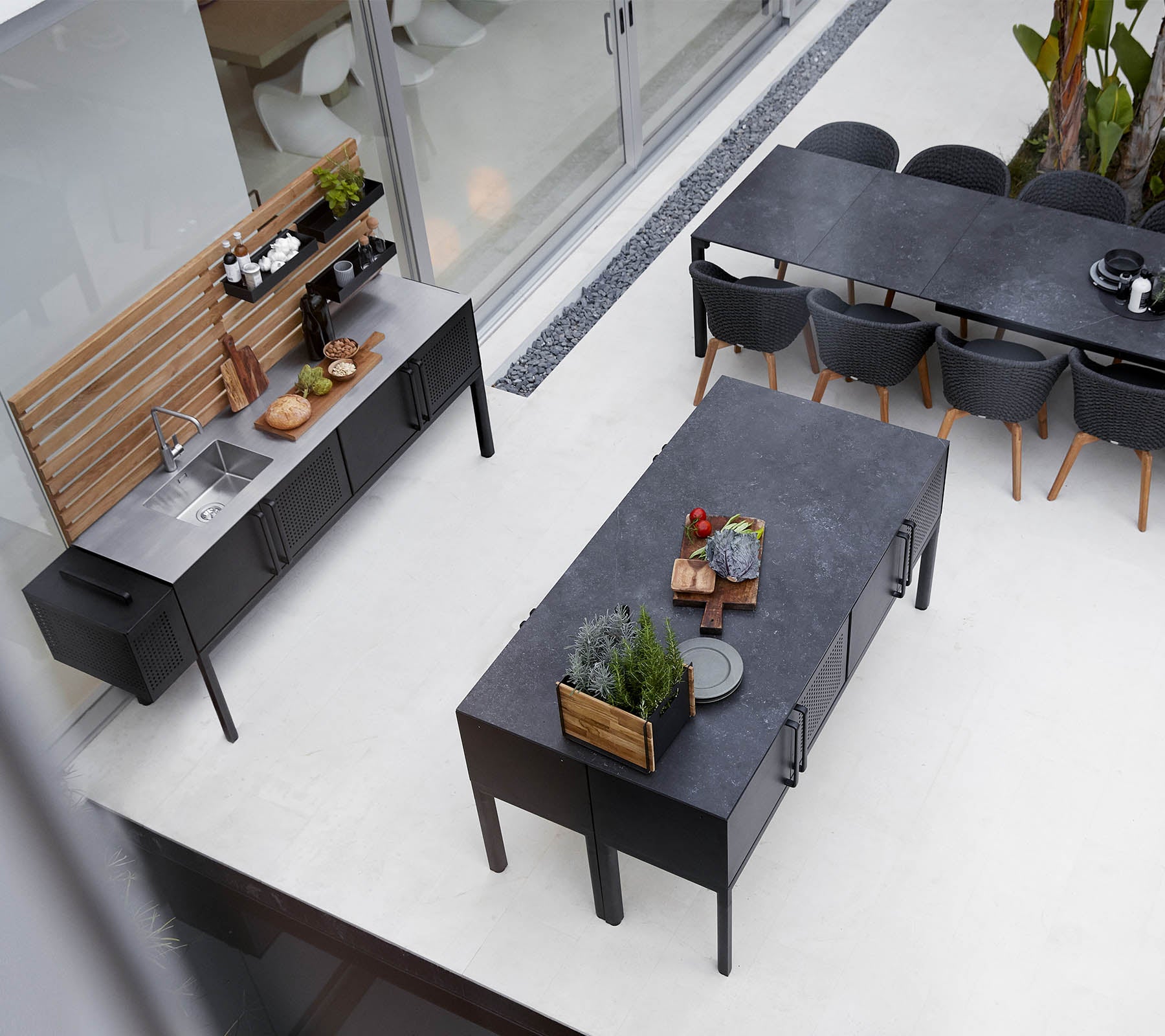 Moderne udendørs køkkenopstilling med en slank bordplade, rummeligt spisebord og stilfuld siddearrangement med planter og dekorative elementer.