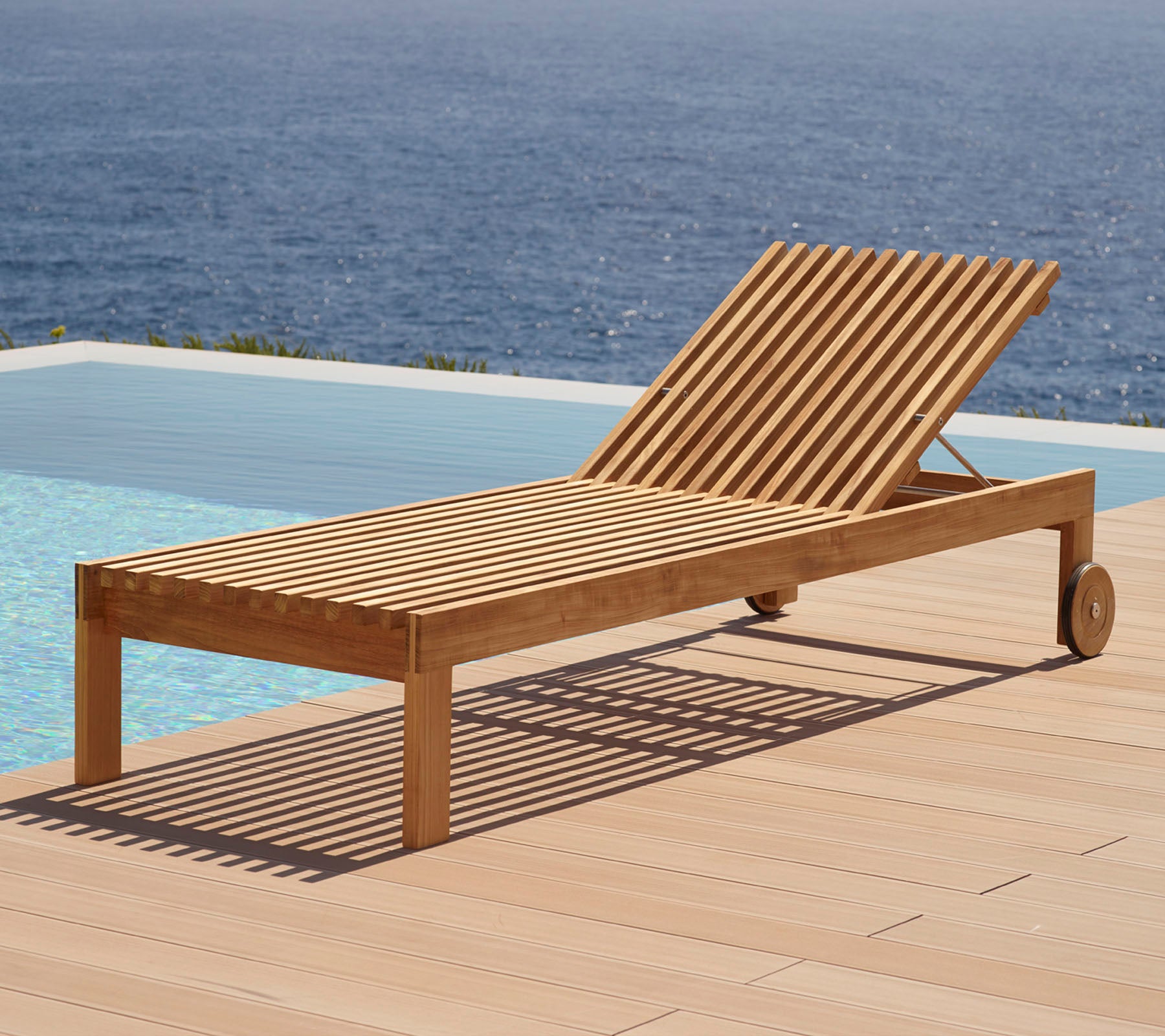Træ-lounge stol med skråbånd design, med hjul og placeret ved en swimmingpool med vandudsigt i baggrunden.