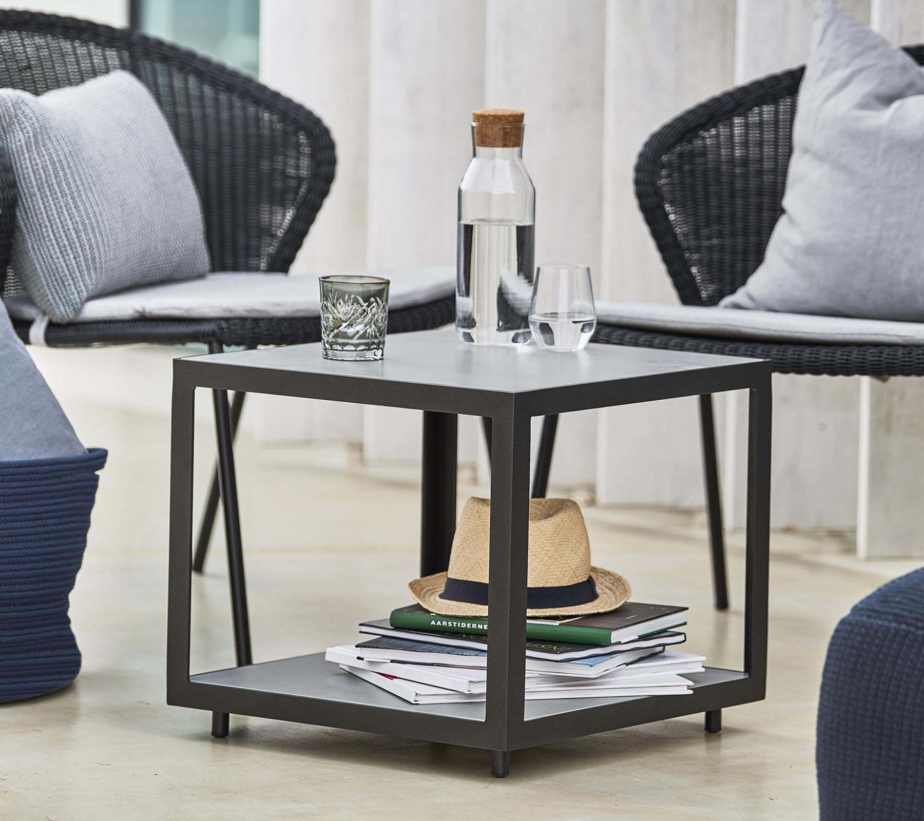 Et moderne bord med en vandflaske, et glas og dekorative genstande, omgivet af stilfulde stoler og puder.