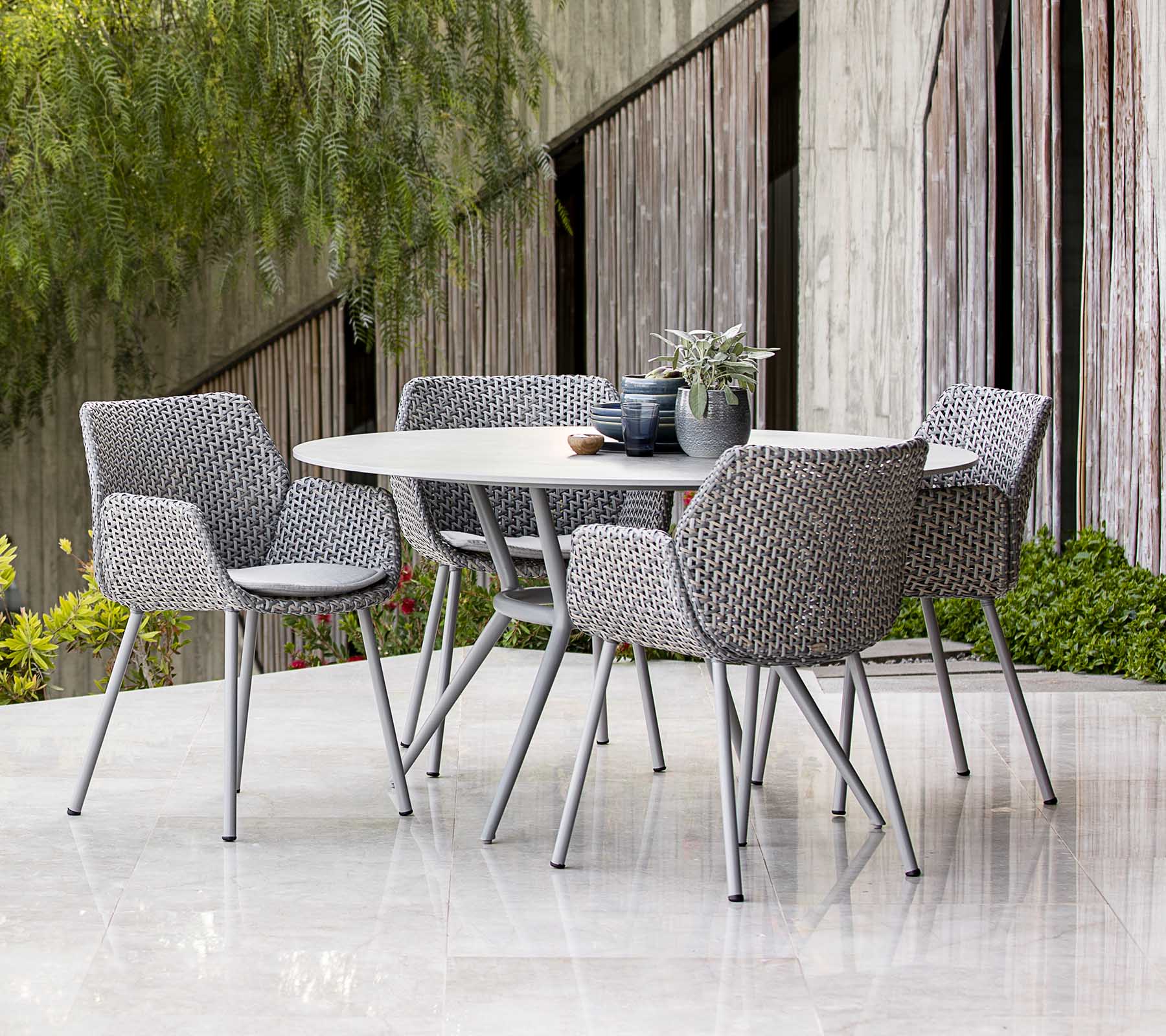 Moderne udendørs spisebord sæt med vævede stole, stylet med planter og borddekoration, med en moderne æstetik.