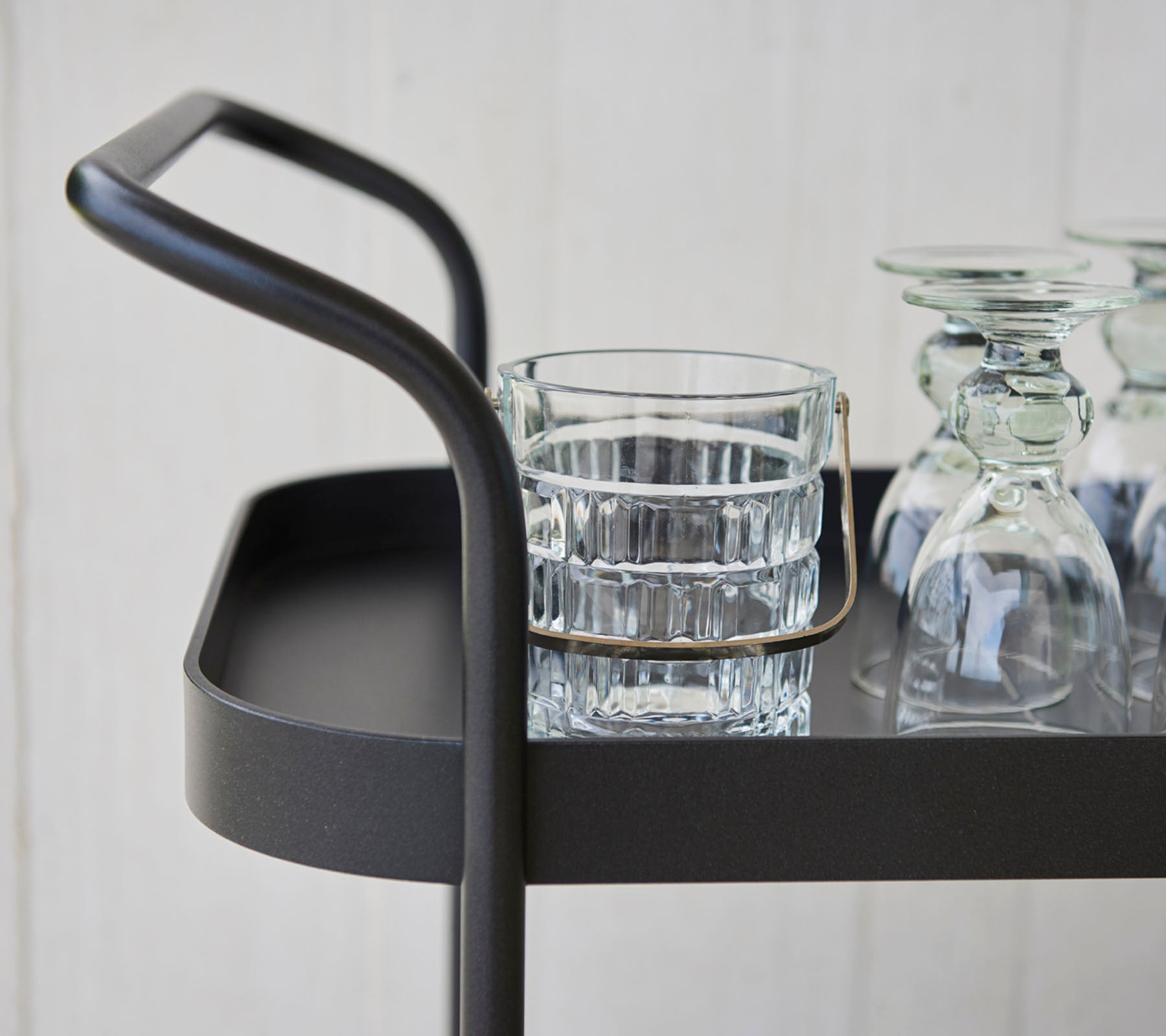 Stilfuld serveringsvogn med et slankt håndtag, der har et glas tumbler og flere klare glasskær på en flad overflade.