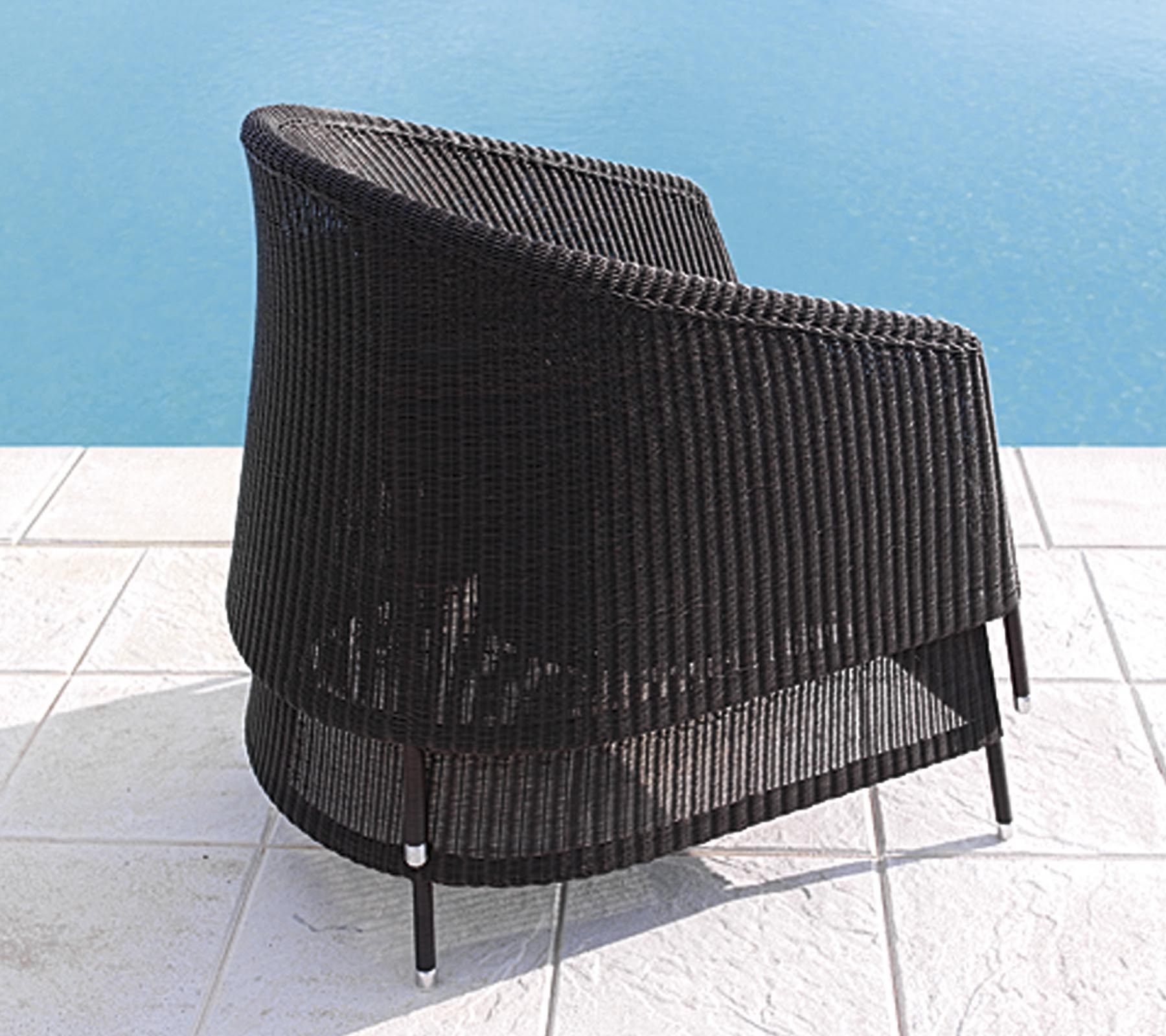 Buet sort rattan stol med et elegant design, placeret nær en pool på hvide flisegulve.