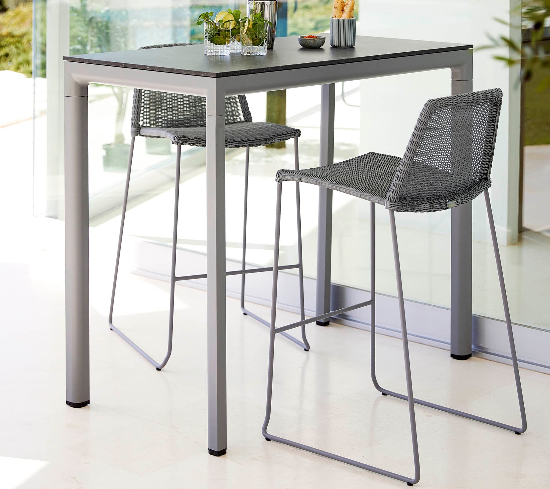 Et slankt bord med to høje barstole, der har et moderne design og lys farveskema, suppleret af en lille plante som centerpiece.