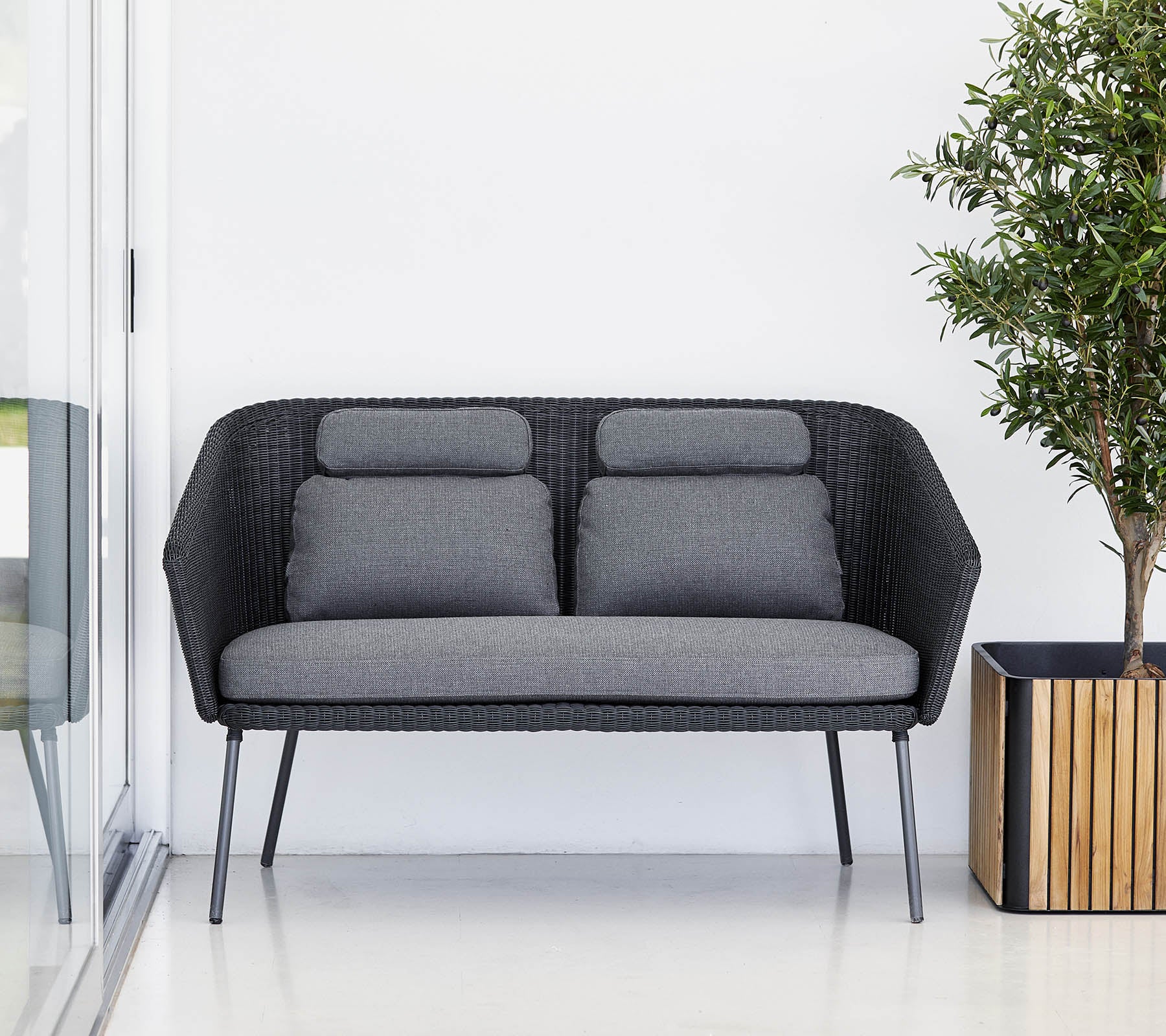 Stilfuld sort sofa med grå puder, suppleret med en potteplante i en trækrukke. Moderne og minimalistisk design.