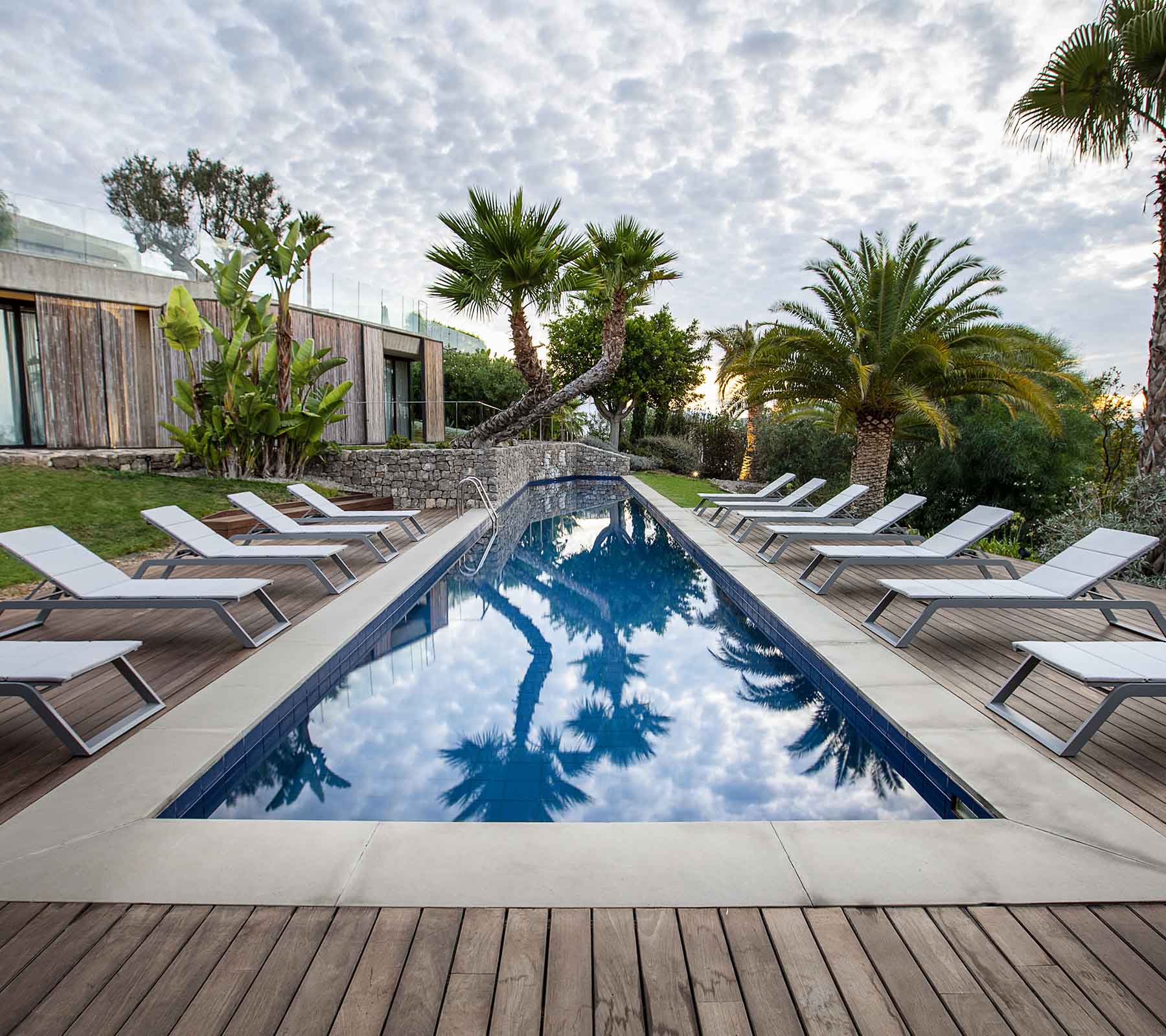 Fredfyldt scene med en pool omgivet af liggestole og palmer, der spejler himlen og den frodige grønne vegetation.