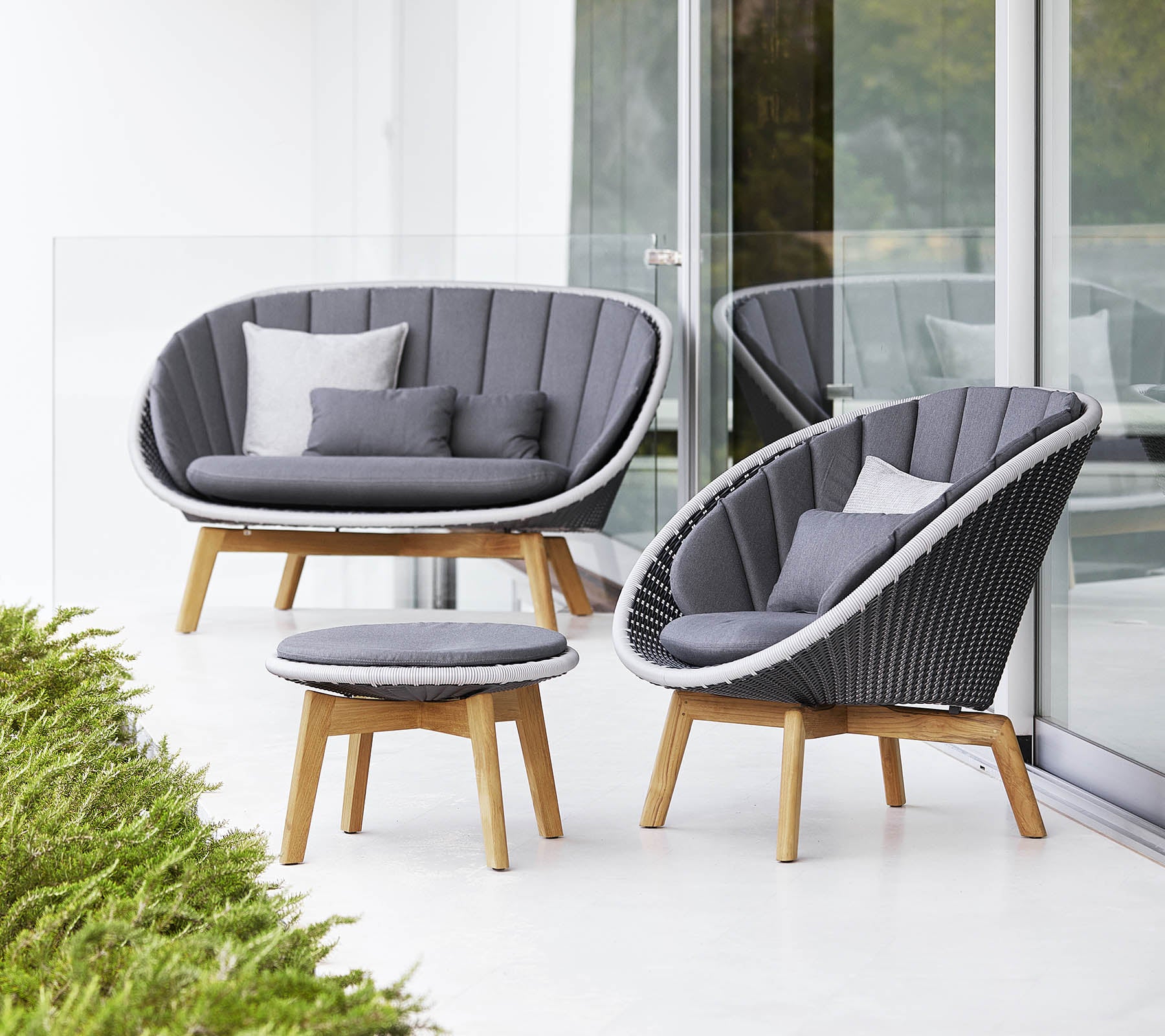 Stilfuldt sofasæt med en buet sofa, stol og rundt kaffebord, alle med et moderne design og bløde grå puder.