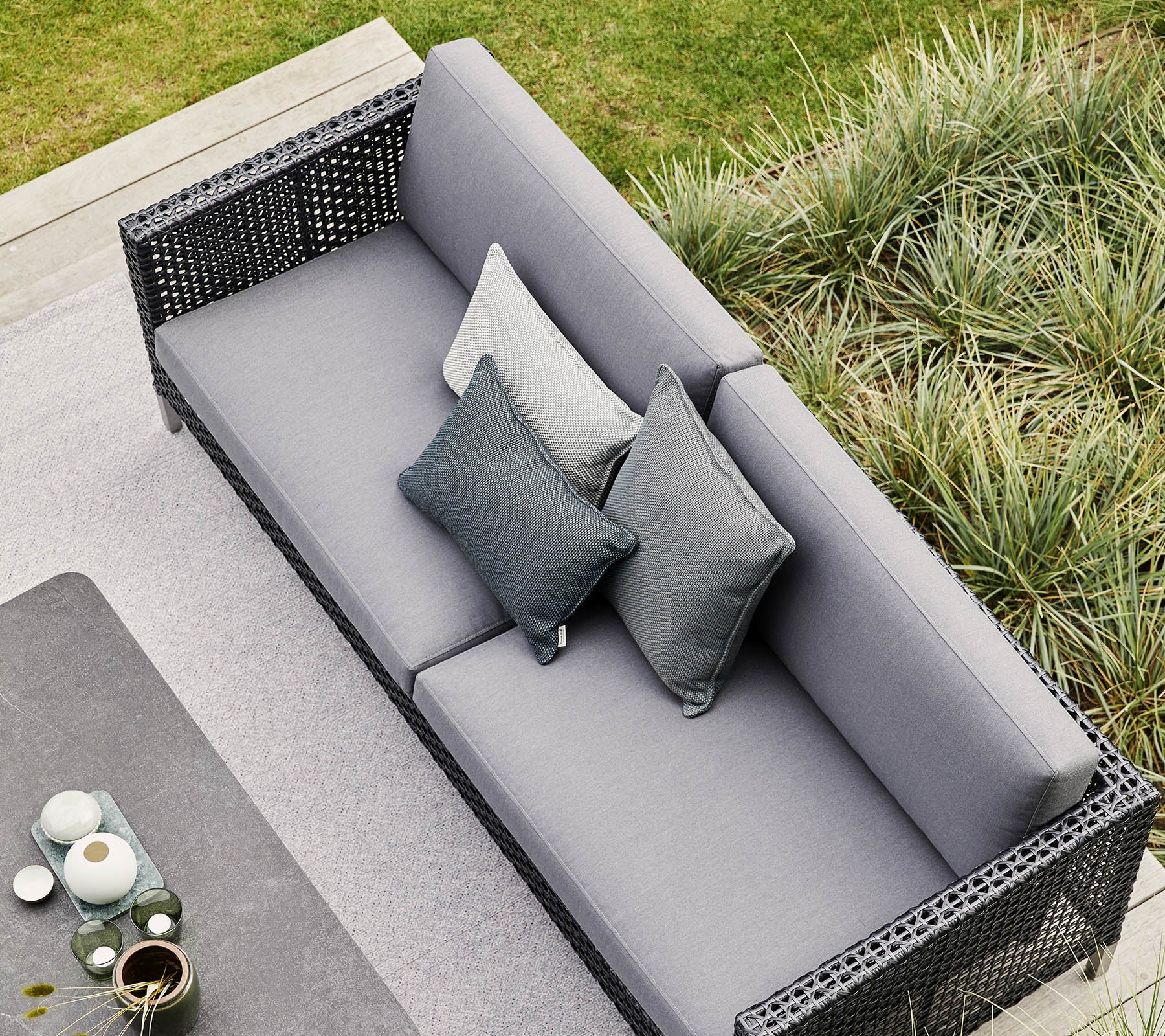 Stilfuld grå sofa med dekorative puder, omgivet af frodig grønne planter og moderne dekorative elementer. Perfekt til afslapning og sammenkomster.