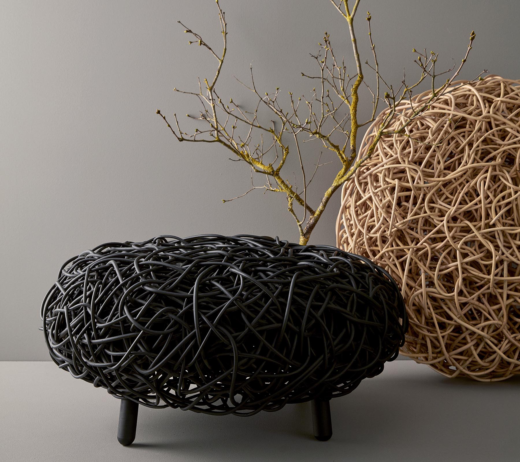 Et stilfuldt, rundt sofabord lavet af vævet materiale, der fremviser sorte og naturlige nuancer, med en dekorativ gren placeret ovenpå.