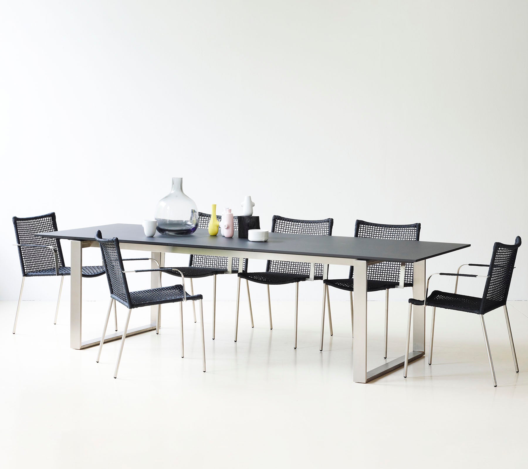 Et moderne spisebord med et strømlinet design, omgivet af stilfulde sorte mesh-stole og dekorative vaser.