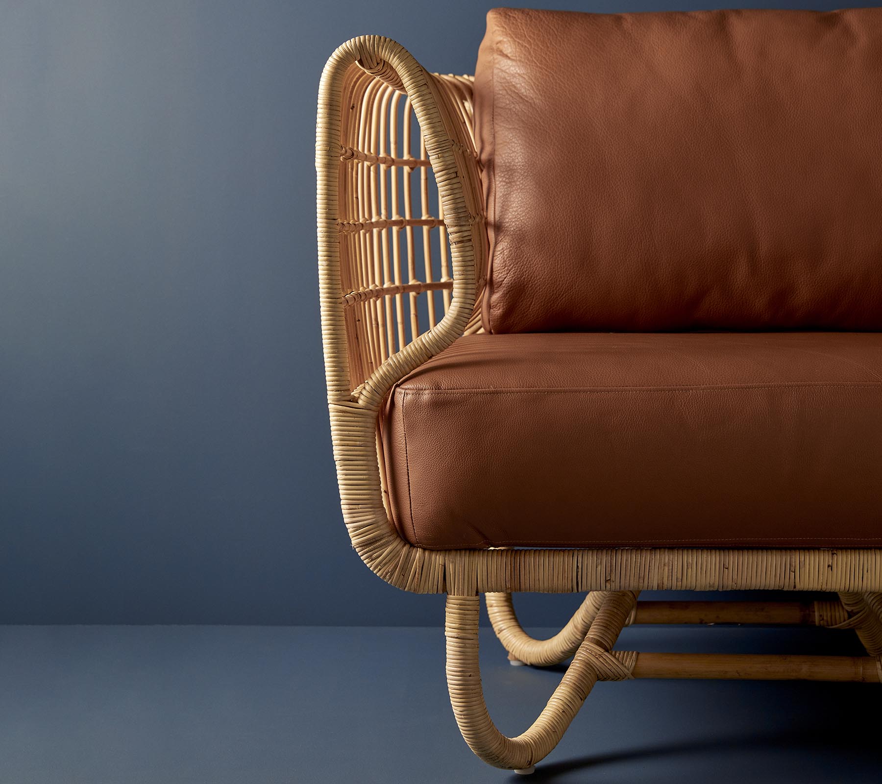 Rattan stol med en båret design og brune læderpuder, der viser en blanding af naturlige materialer og moderne æstetik.