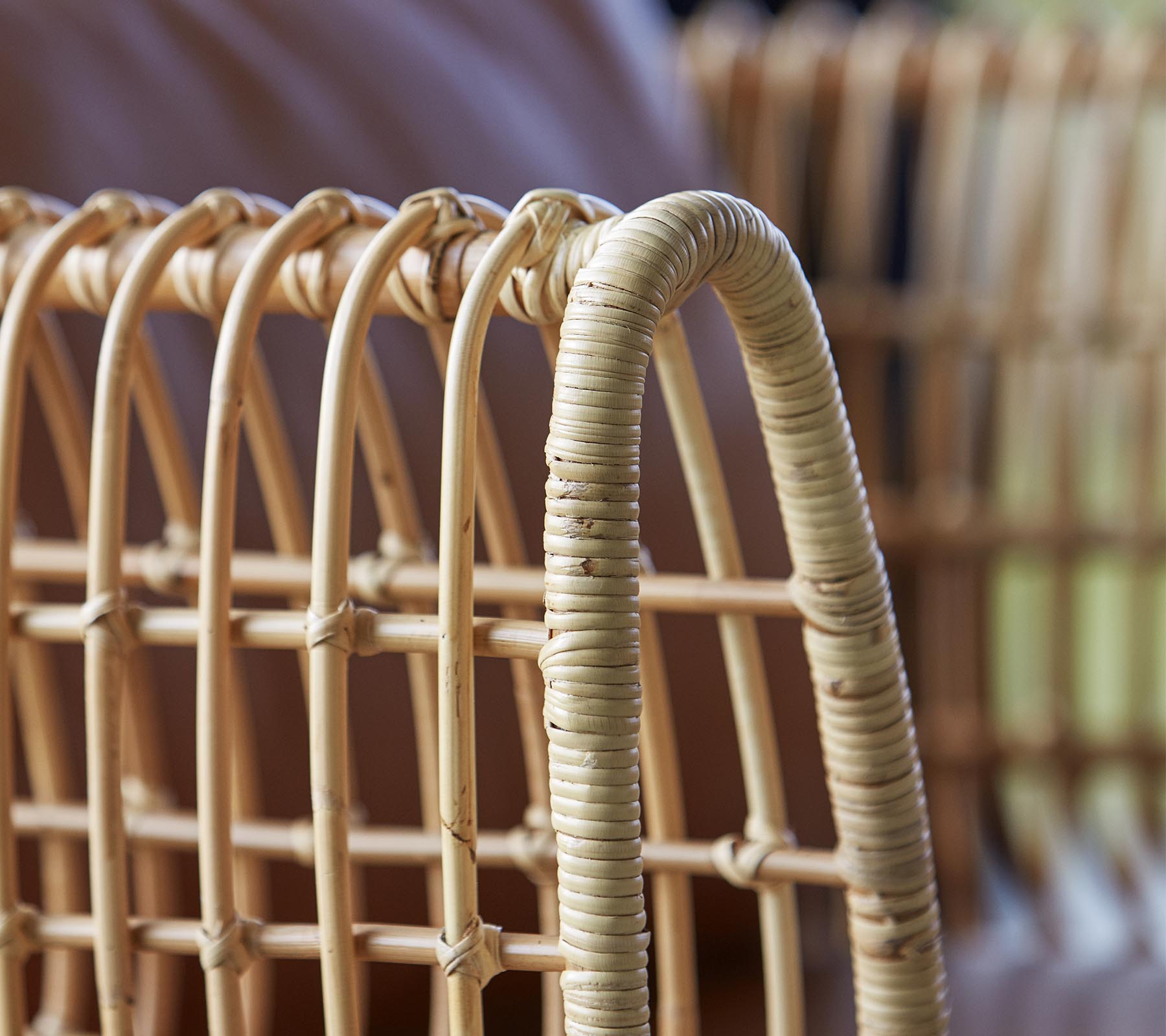 Nærbillede af en vævet rattan stol med buede linjer og en naturlig finish, der fremhæver dens håndværk og design.