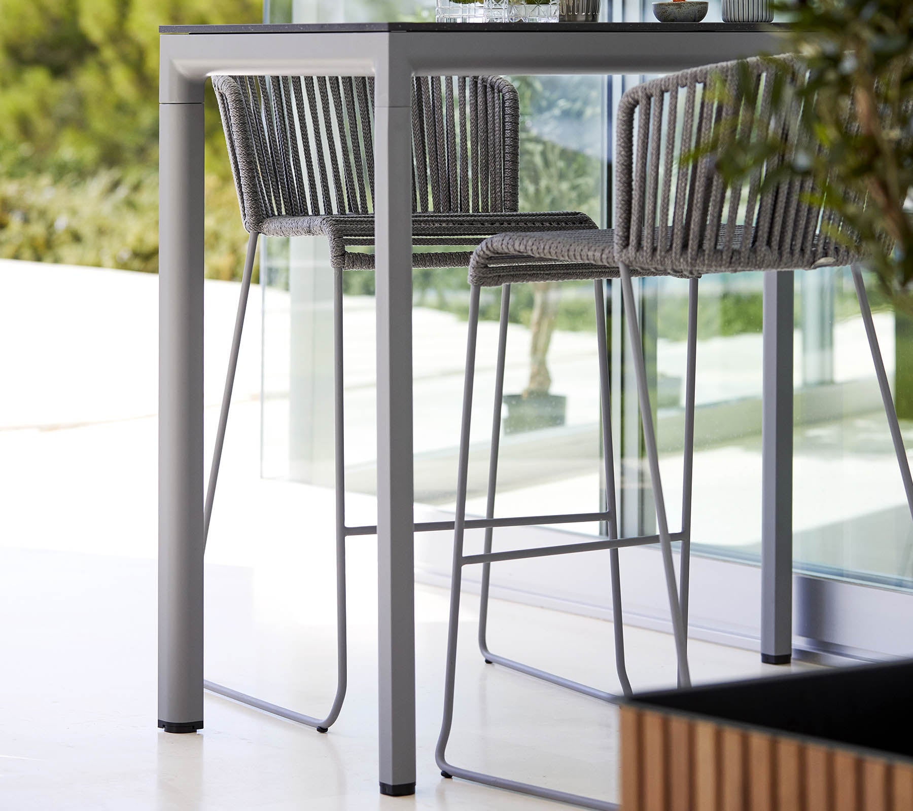 Et slankt, moderne bord med matchende højstole, der har et minimalistisk design og en stilfuld metalramme, komplementeret af naturlig grønne planter.