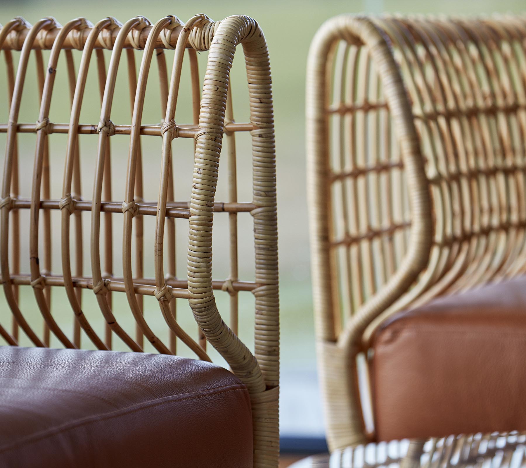 To stilfulde stole med vævede rattan rygge og glatte lædersæder, der viser en moderne designæstetik.