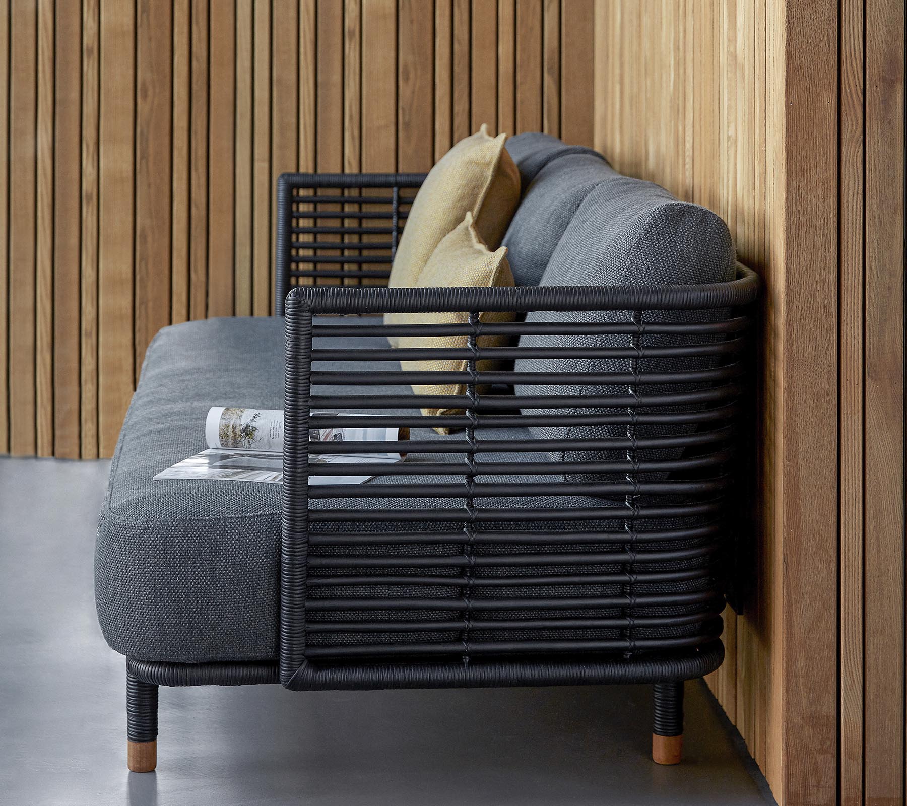 Stilfuld sofa med et slankt design i en tekstureret grå stof og dekorative puder, suppleret af en moderne lamelframme.