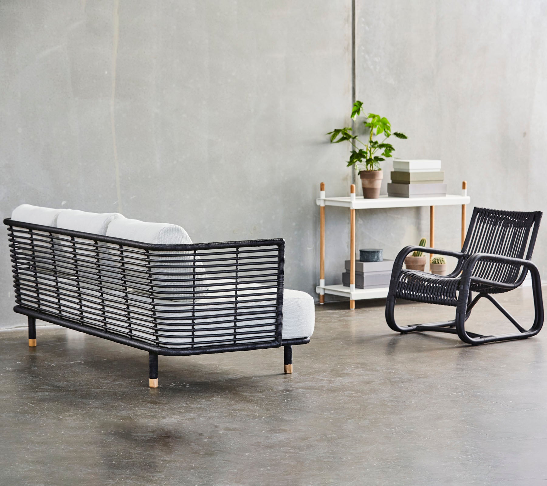 En moderne siddearrangement med en stilfuld sort rammesofa med hvide puder og en matchende gyngestol, fremhævet af grønne planter.