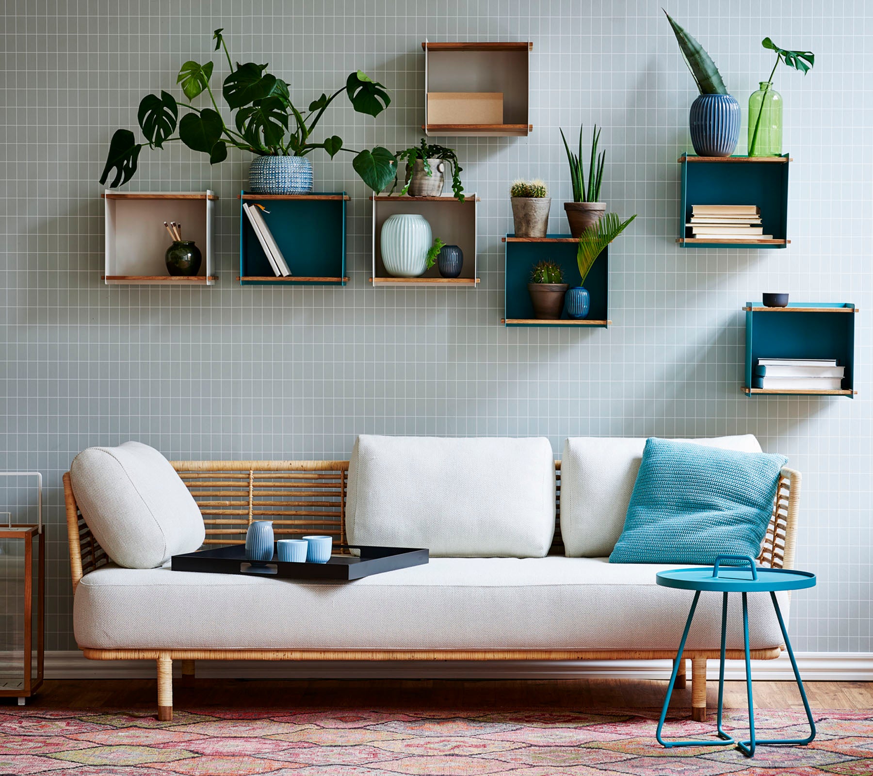 En stilfuld sofa med et let pudebetræk og et lille bord, prydet med forskellige potteplanter placeret på geometriske hylder.