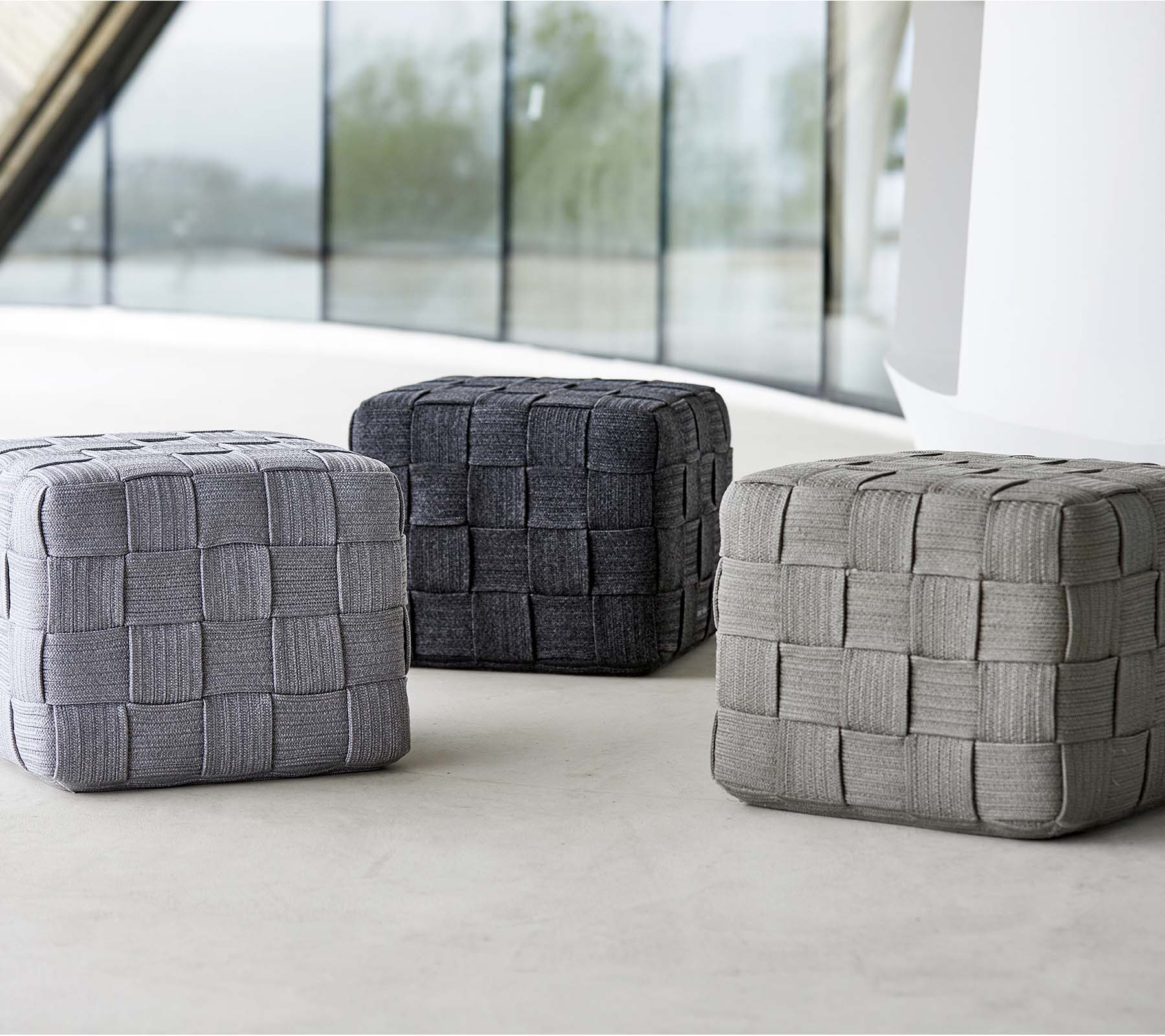 Tre vævede pouffer i forskellige nuancer af grå, med et struktureret design, arrangeret på en lys overflade. Ideelle til siddepladser eller dekoration.