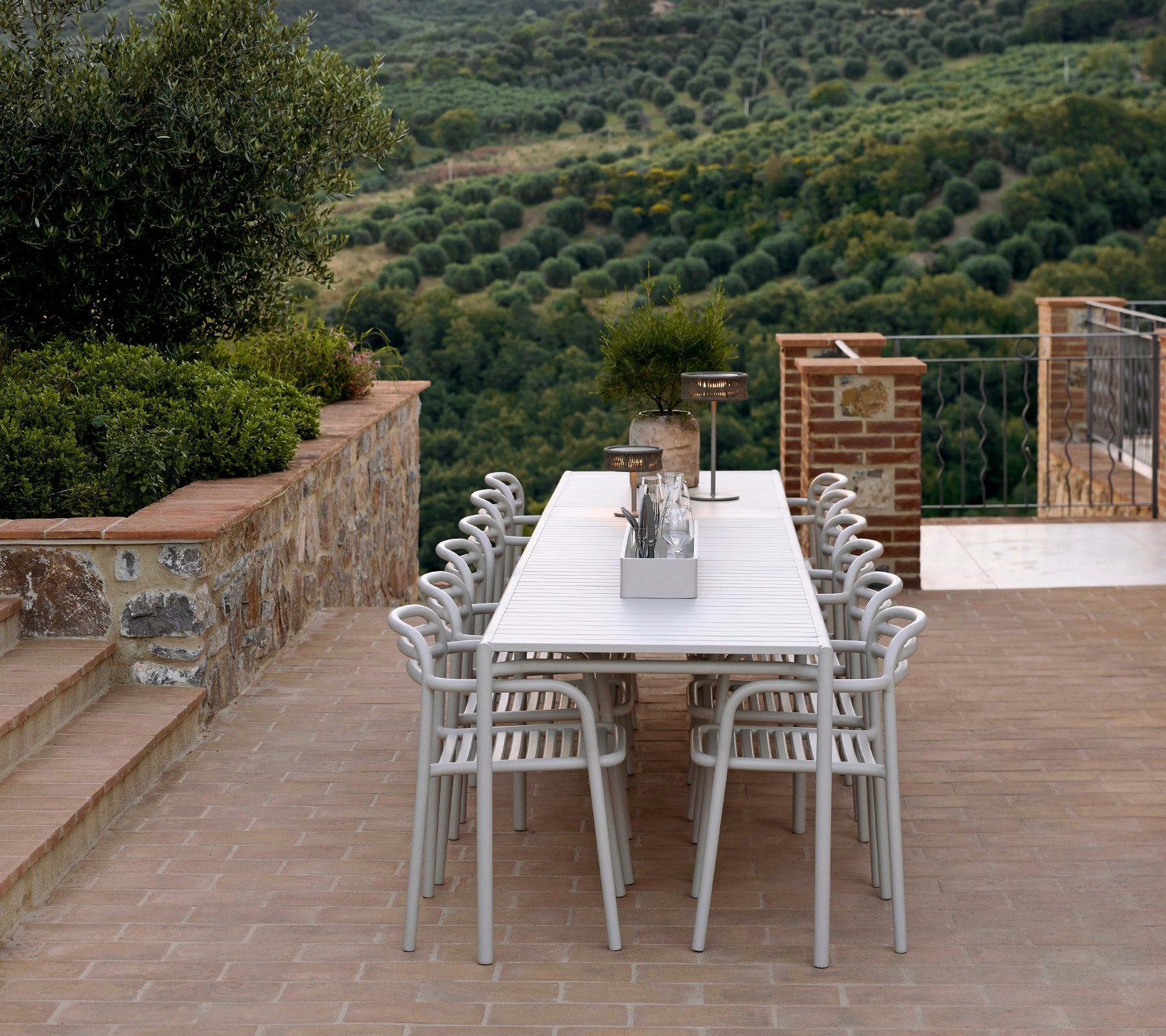 Et stilfuldt siddemiljø med Bliss-stole og bord i sandfarve, suppleret af en Illusion-lampe, omgivet af et frodigt landskab.