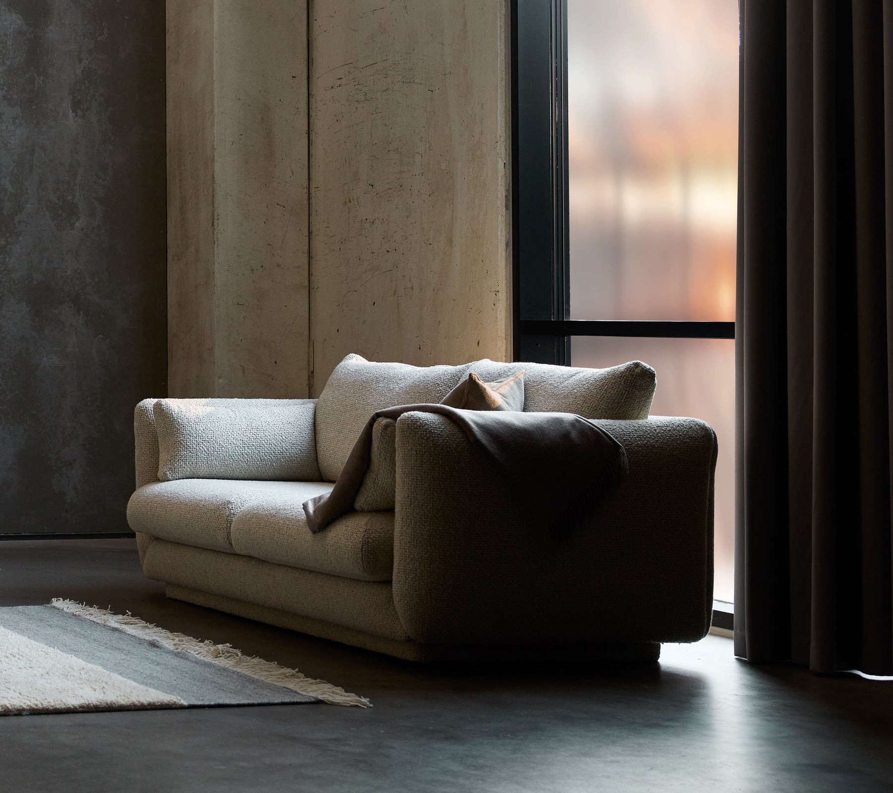 Bloom 2-personers sofa i sandfarvet flair, med en sokkel-design og en hyggelig plaid draperet over den ene side.
