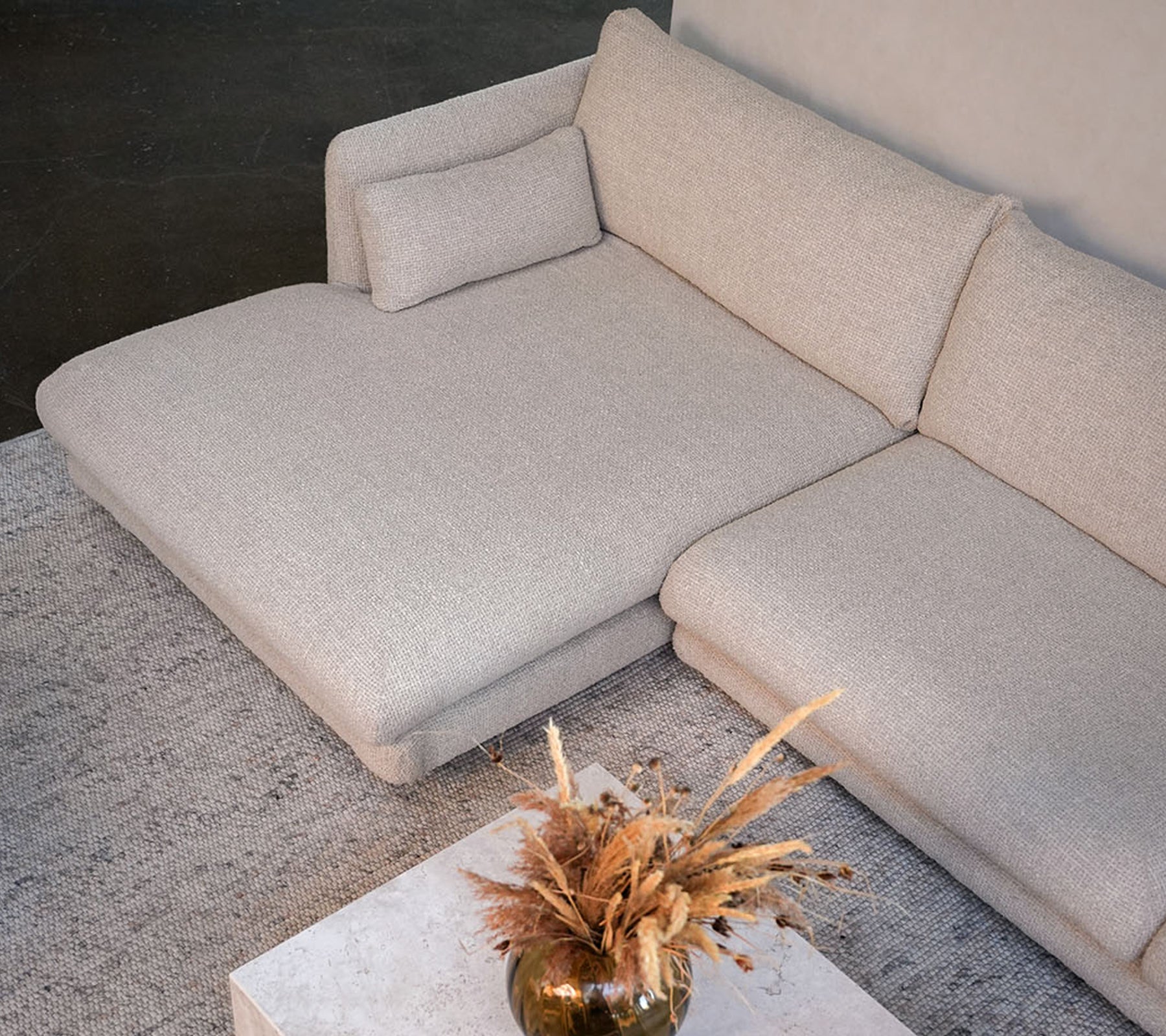 Moderne beige sofa med et hvidt bord og en dekorativ vase i en stilfuld loungeindstilling.