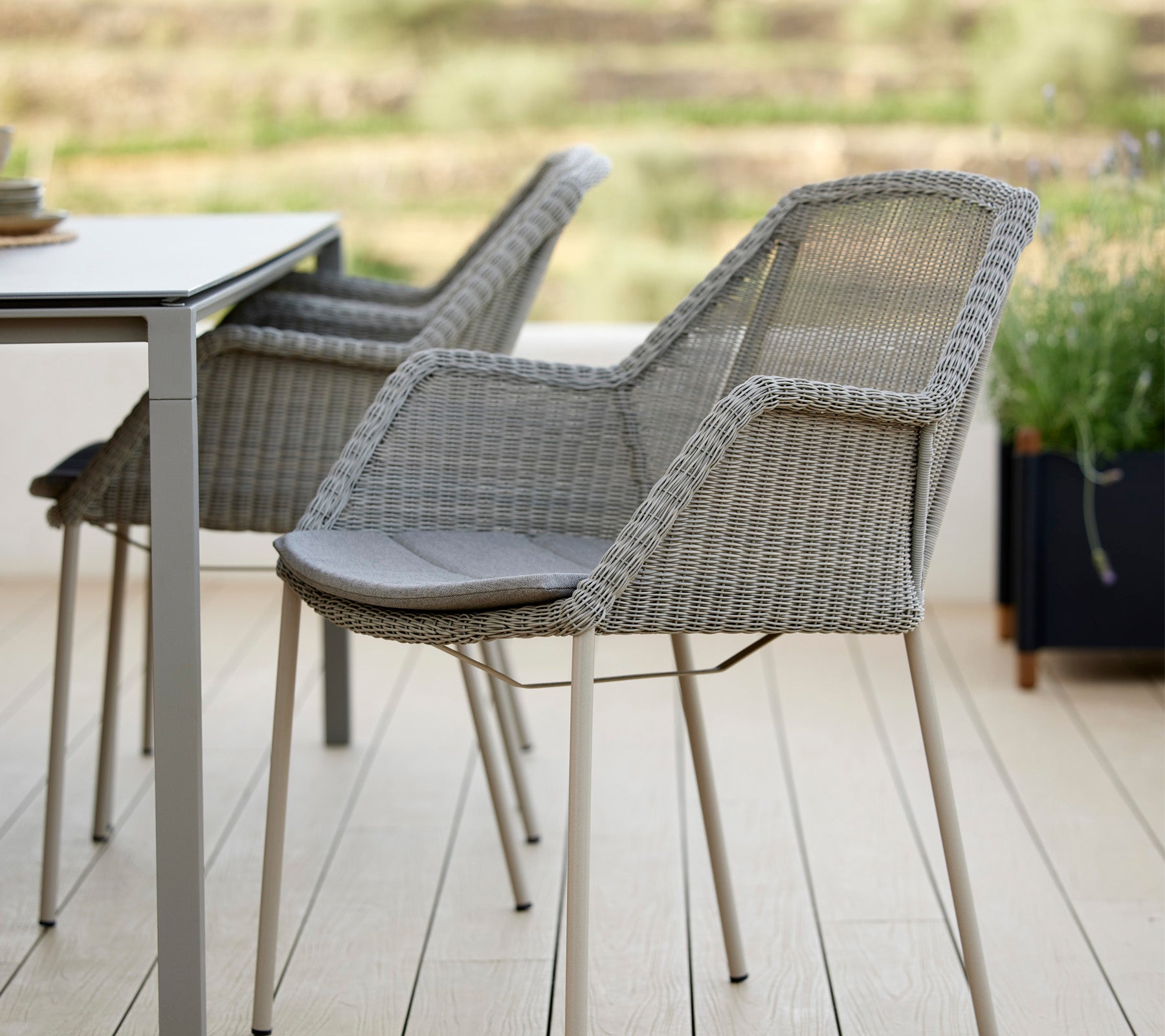 To stilrene vævede stole ved siden af et moderne bord, der har et slankt design og komfortable puder, ideelt til afslapning i en fredfyldt omgivelser.