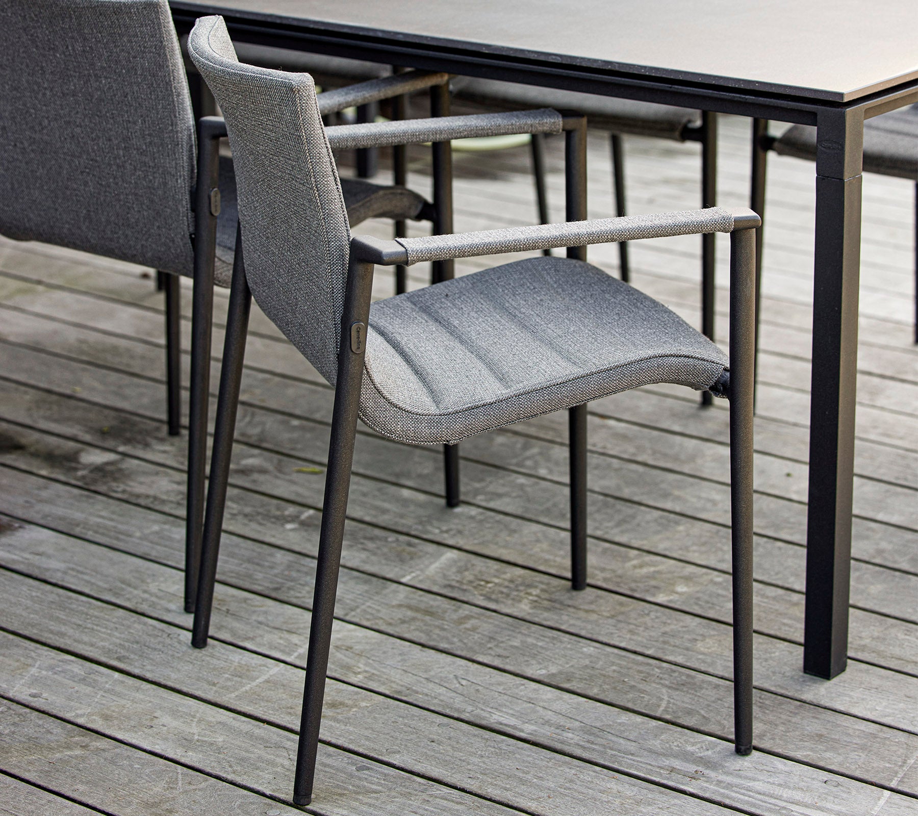 Stilfuld grå stol med armlæn placeret ved siden af et elegant sort bord på en træoverflade. Ideel til moderne udendørs miljøer.