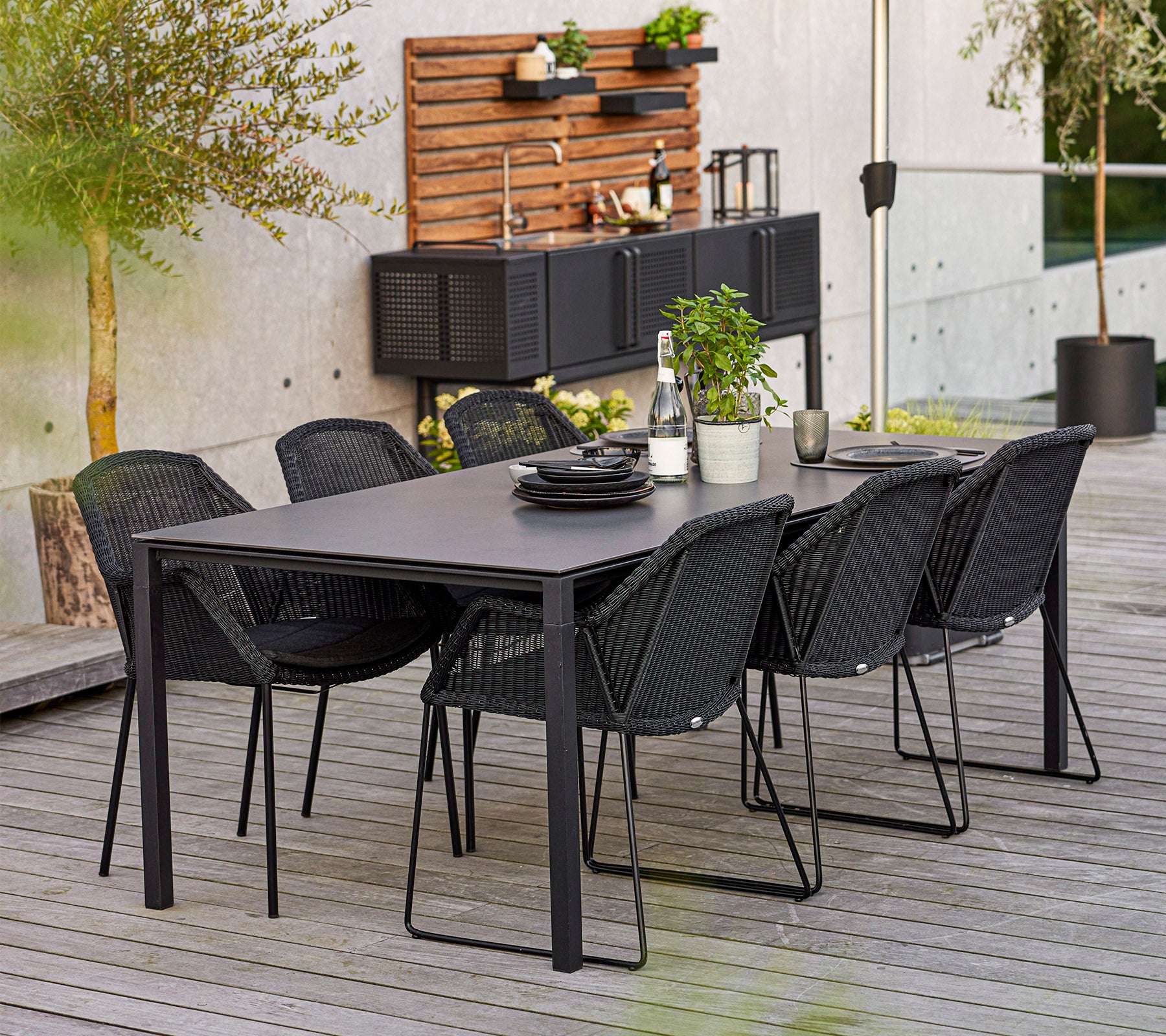 Et moderne spisesæt med et rektangulært bord og seks stilfulde stole, suppleret med dekorative planter og tallerkener.