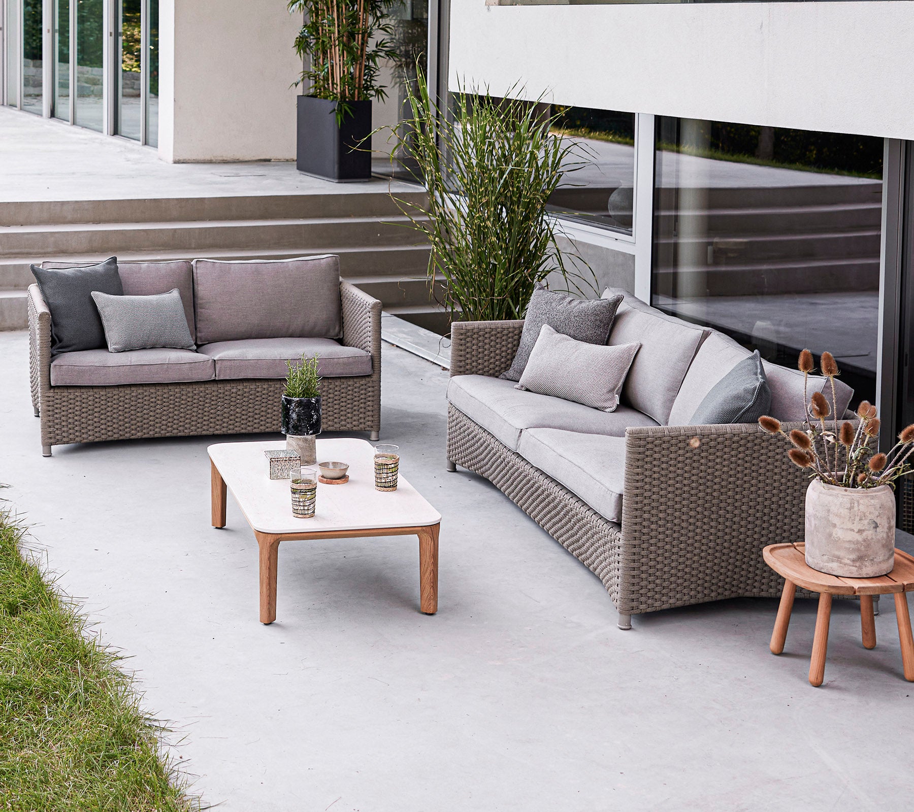 Moderne udendørs siddeplads arrangement med en sofa, en kærlighedssofa og et kaffebord med dekorative elementer. Stilfuld og indbydende atmosfære.