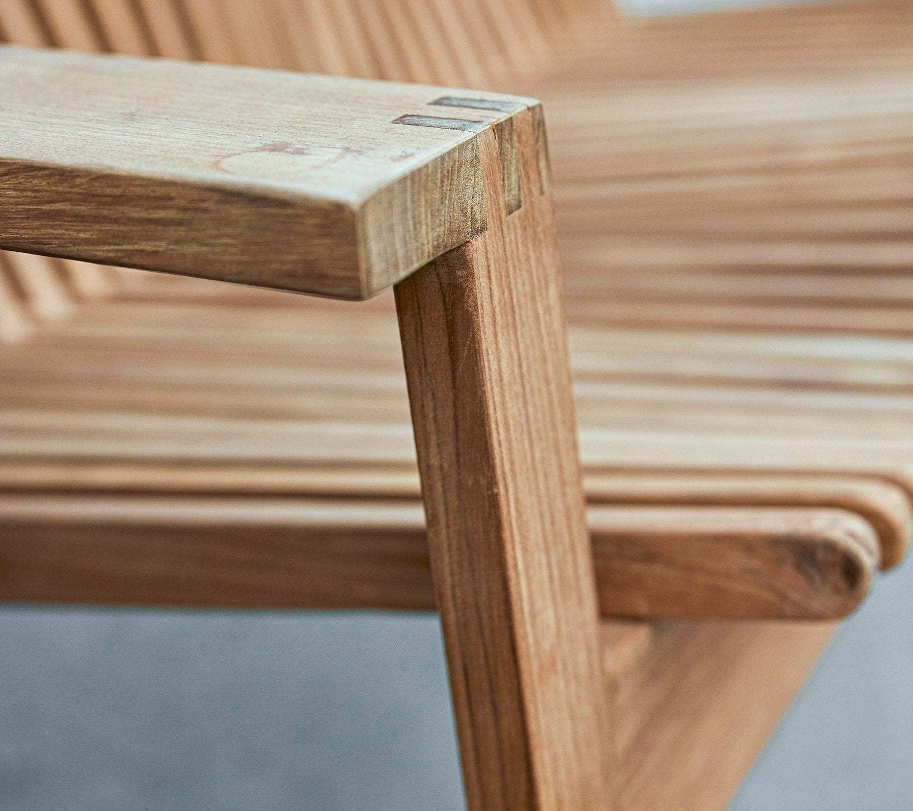 Nærbillede af en træstol armstøtte, der viser et slankt design med lamelbeskæret sæde og glatte overflader.