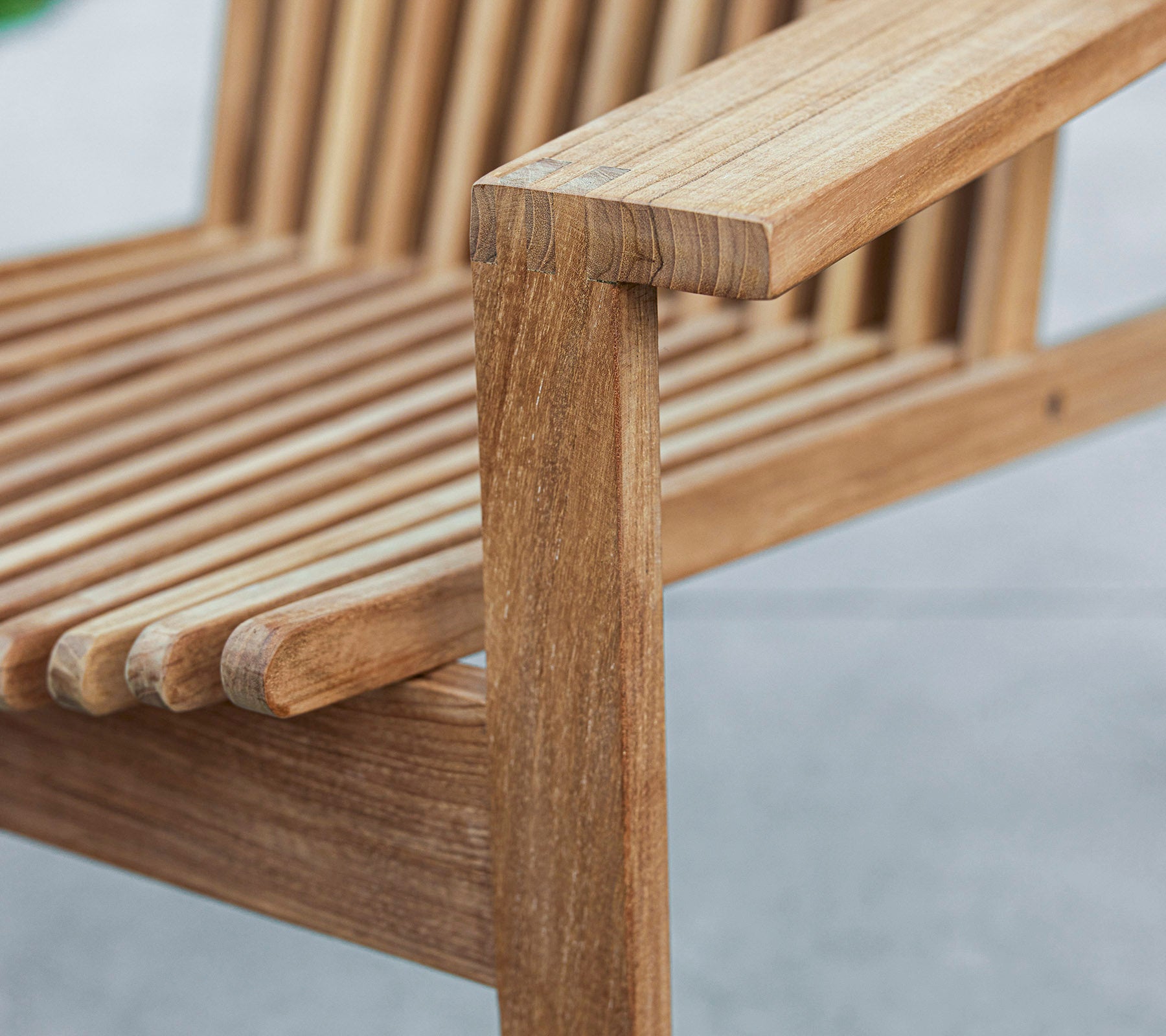 Nærbillede af en træbænk med en skridsikker design og en robust armlæn, der fremviser naturlige træårer og håndværk.