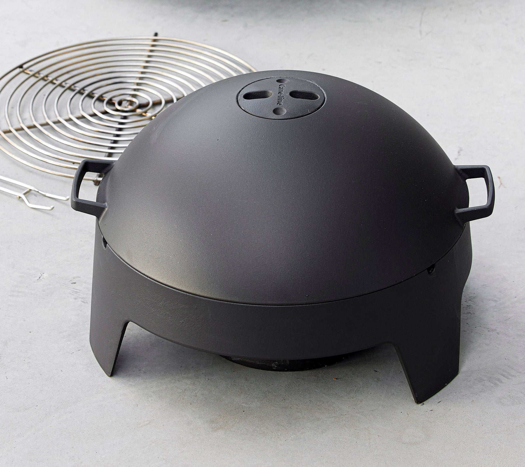 En slank sort madlavningsapparat med en kuppelform og håndtag, ledsaget af en cirkulær grillrist. Ideel til grillning og udendørs madlavning.