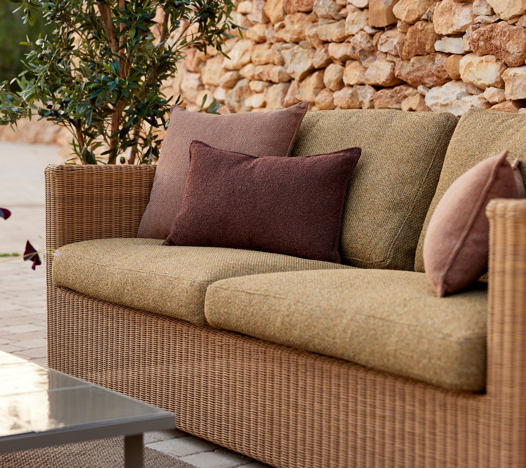 Moderne beige sofa med lilla og brune puder i et loungeindstilling.