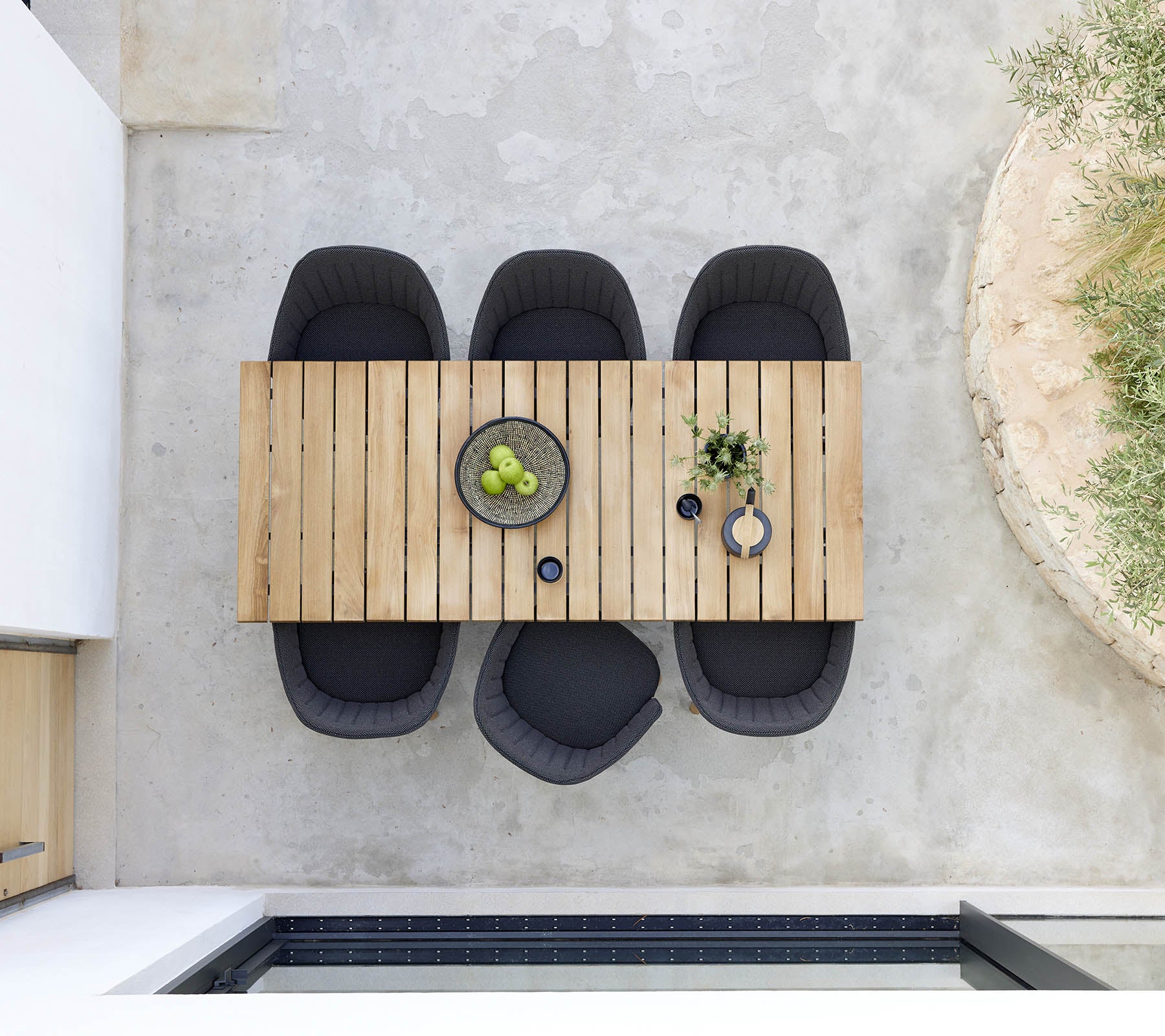 Elegant træspisebord ledsaget af fire sorte stole, med en skål med grønne frugter og dekorative planter for et moderne præg.