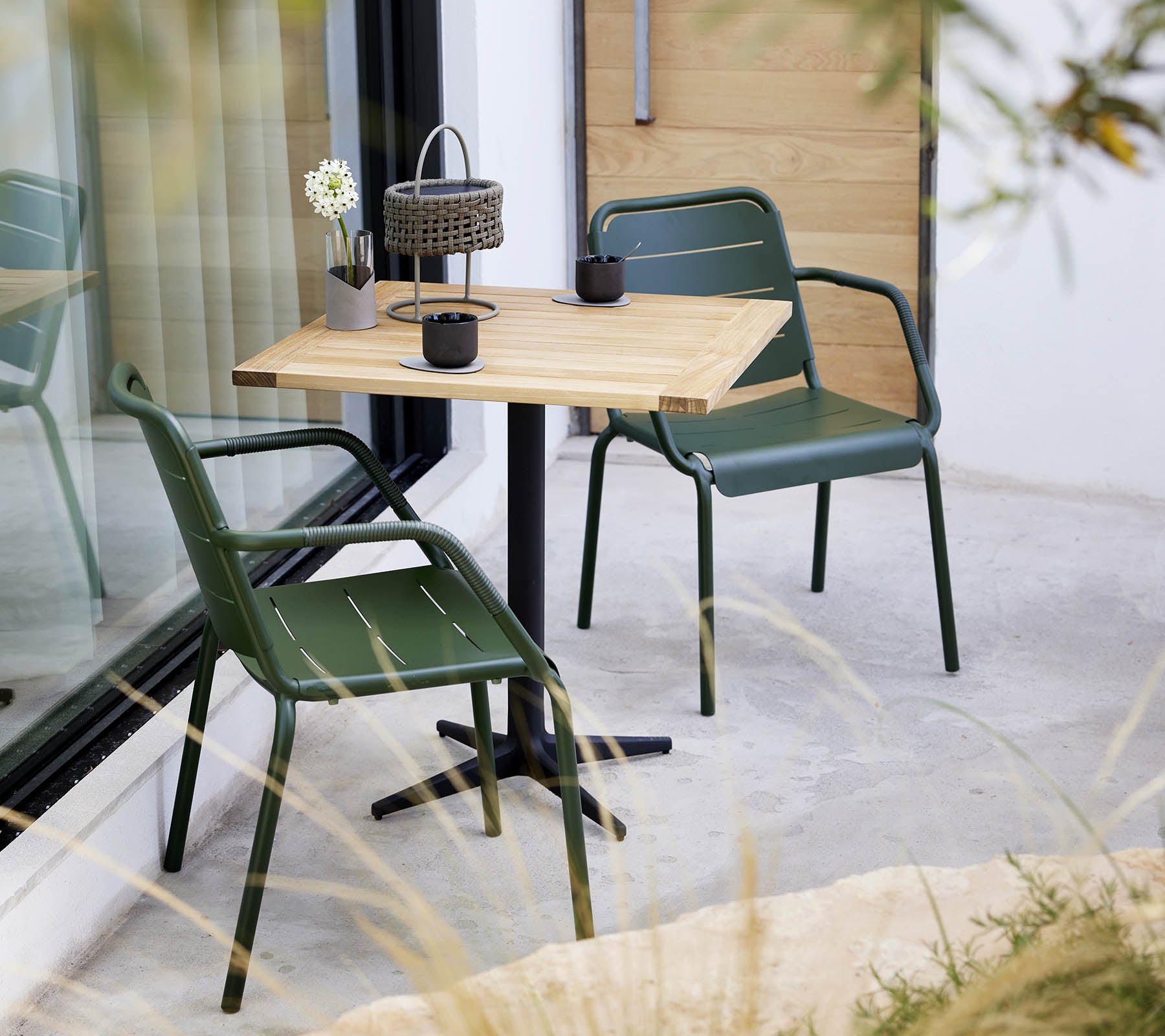 Et minimalistisk miljø med et træbord og grønne stole, med en lille blomsterarrangement og dekorativ lanterne.