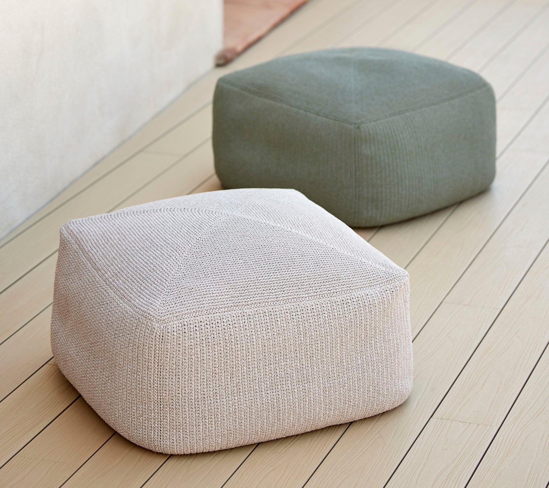 To stilfulde, teksturerede poufs i neutrale toner, en hvid og en grøn, arrangeret på en glat overflade, ideel til alsidig siddeplads.