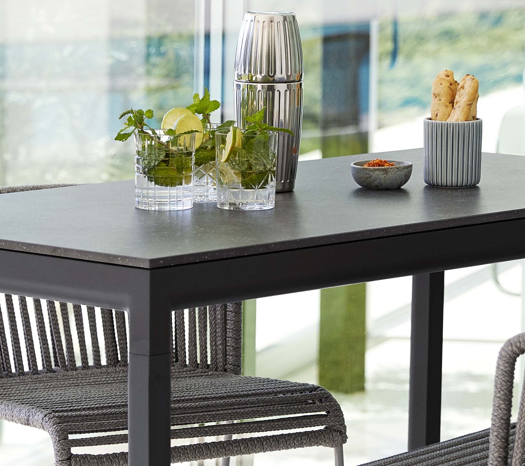 Et moderne bord sat med planter i glasvaser, en dekorativ beholder og en skål med snacks, omgivet af stilfulde stole.