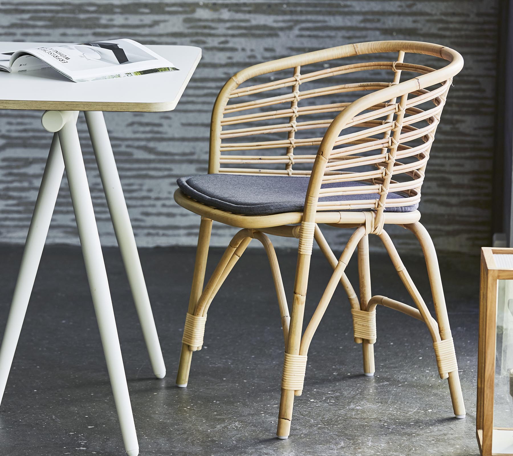 Stilfuld rattan stol med en grå pude, parret med et enkelt bord og moderne dekoration. Egnet til afslappende siddepladser og afslapning.