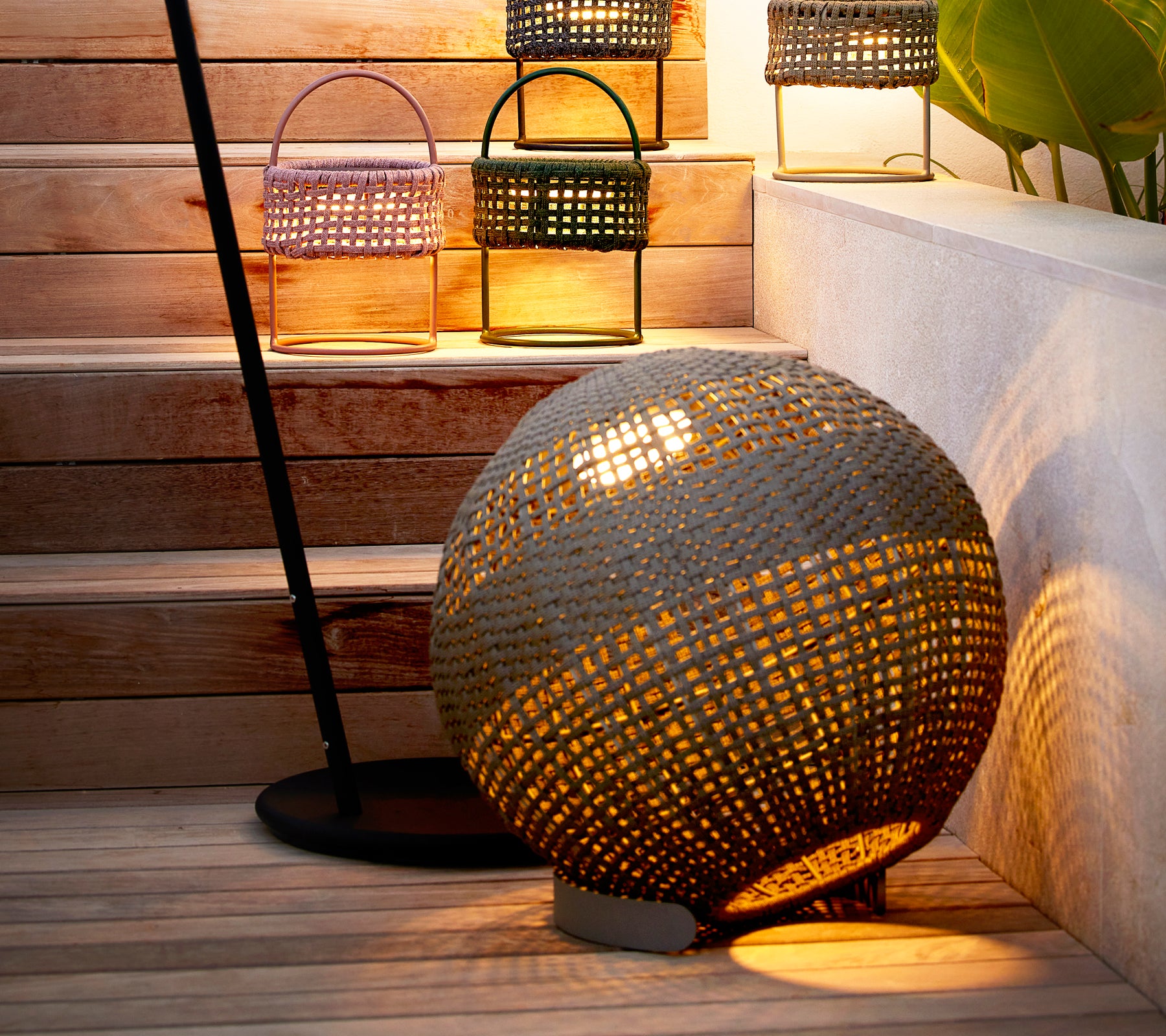 Rund taupe illusion lampe med et vævet design, der kaster et varmt lys ved stilfulde lanterner på en trappe.