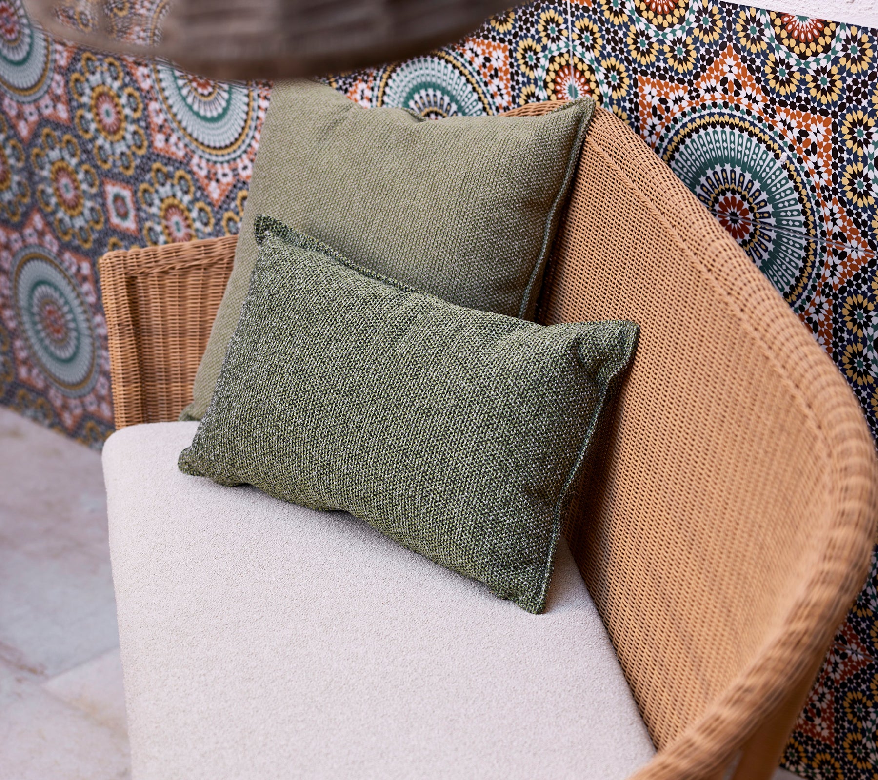 To grønne scatterpuder på en lysfarvet sofa, placeret mod en livlig, mønstret baggrund med cirkulære design.