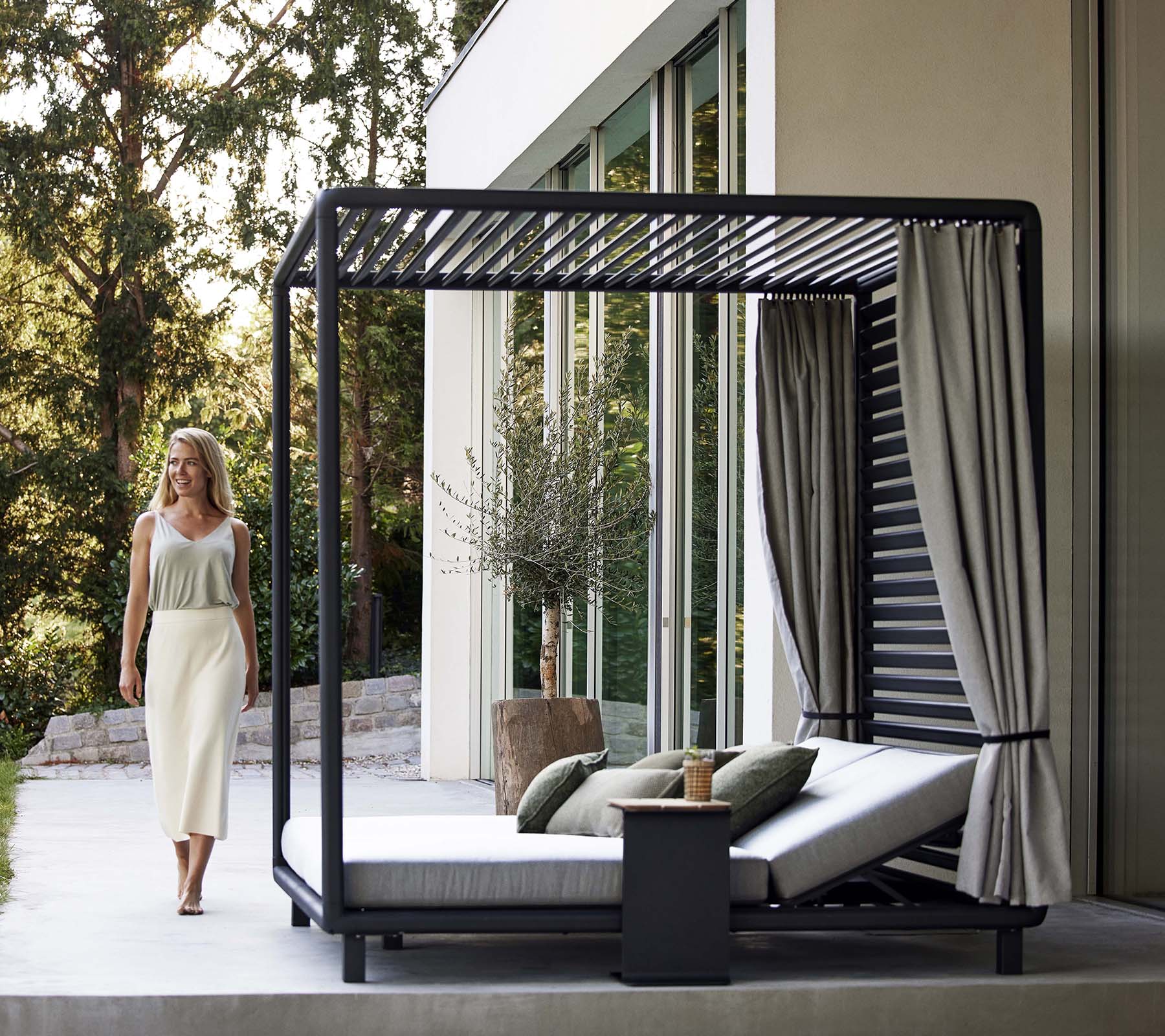 En stilfuld cabana med et glat design, bløde puder, gardiner og et lille sidebord, placeret i en fredfyldt, naturlig omgivelser.