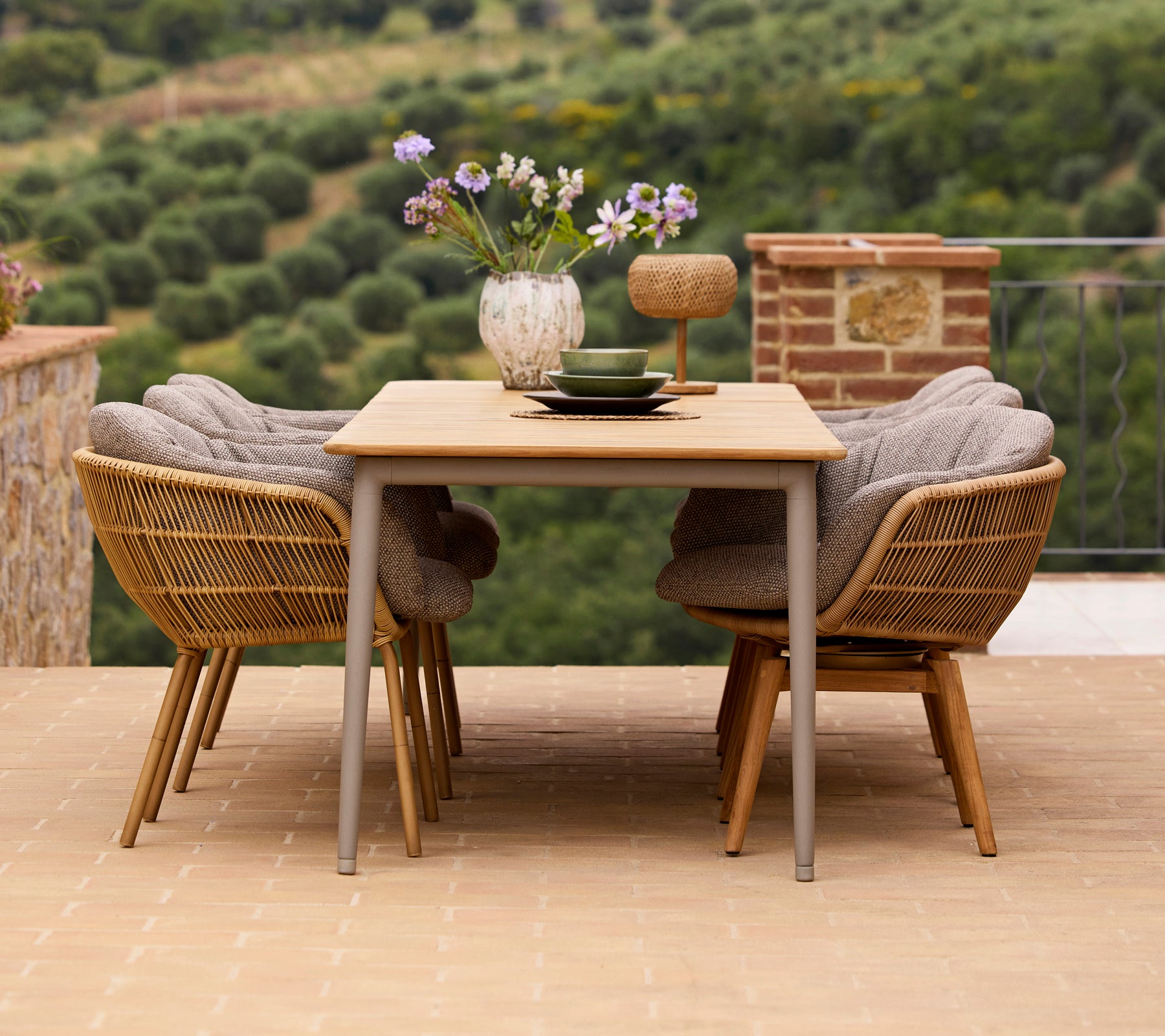 Stilfuld spiseopsætning med et træbord, to Stay-stole med aluminiumsben og en vase med blomster samt dekorative tilbehør.