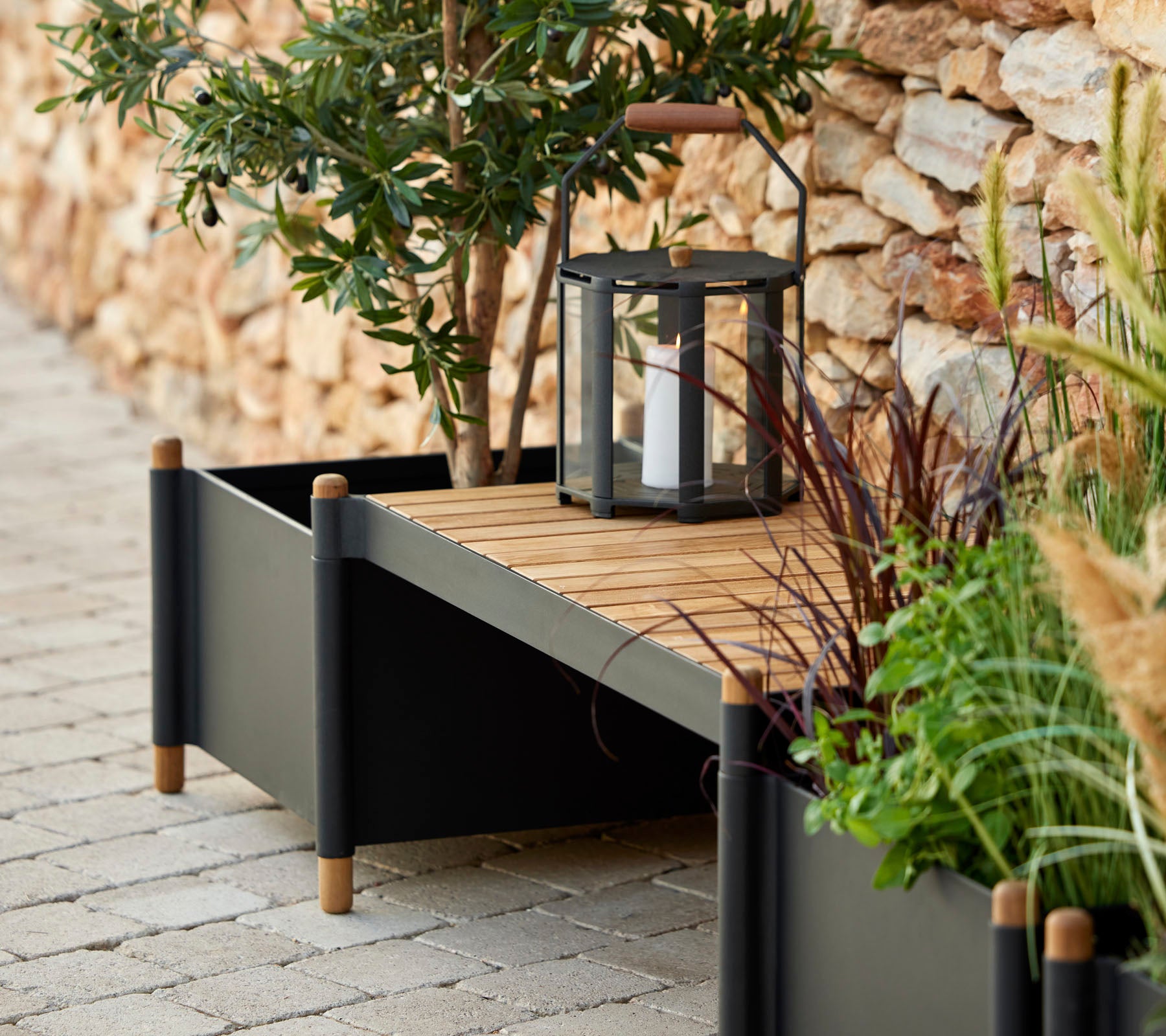 En stilfuld plantekasse med trælameller, omgivet af grønne planter og en lanterne, der tilføjer elegance til rummet.