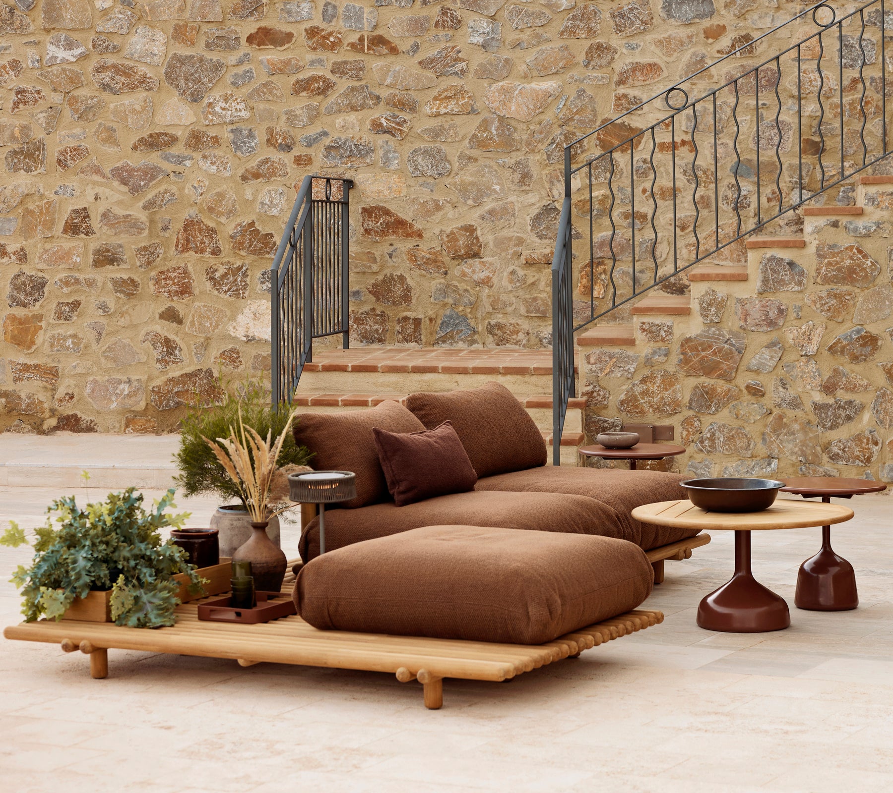 Teak lounge med bløde puder og et Glaze kaffebord, suppleret med dekorative planter og en struktureret stenvæg.