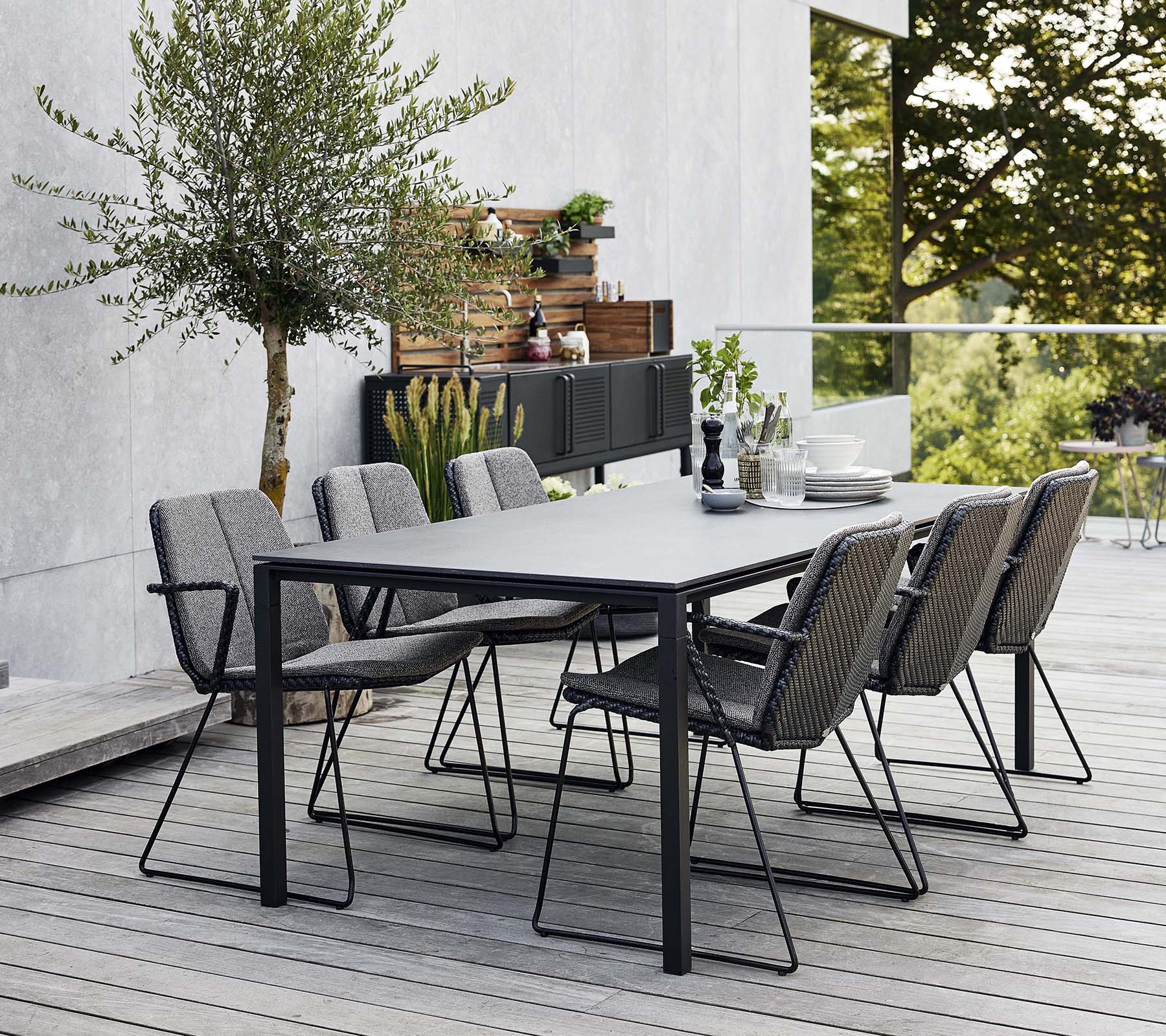 Et stilfuldt udendørs spisebord i moderne design med flere komfortable lænestole, omgivet af grønt og en moderne baggrund.