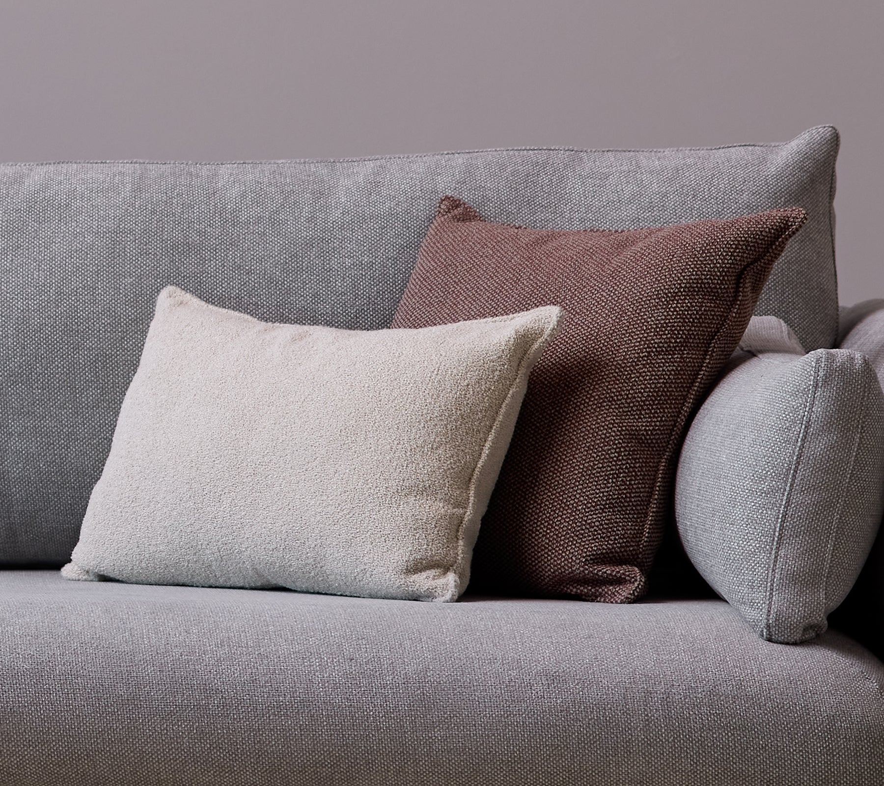 En hvid Scent scatterpude og en Wove mørkerød pude er placeret på en grå sofa.