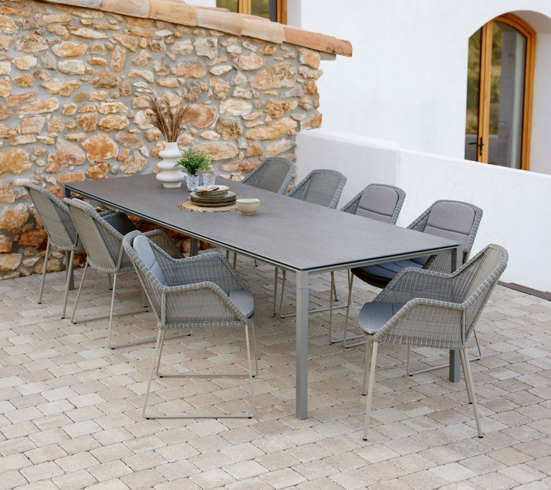 Moderne spisestue med taupe farvede stole, dekoreret med genstande og et strejf af grønne planter mod en stenvæg.