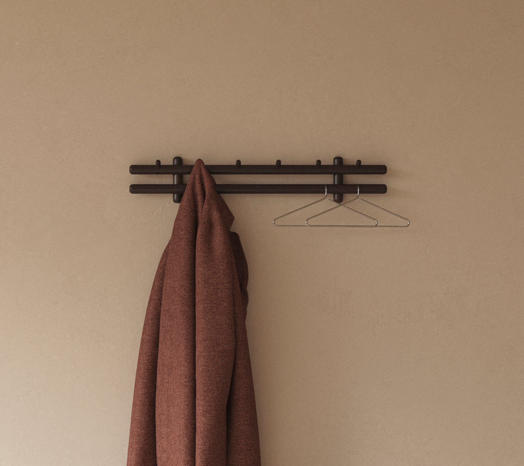 En brun frakke hænger fra en minimalistisk væghylde med kroge, suppleret af en enkel trådholder mod en neutral baggrund.