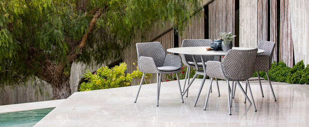 Moderne haveindretning med gråt flettet havestole om rundt bord, spisebordsmøbler ved poolområdet i haven