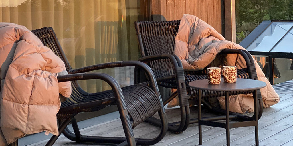 To Curve loungestole i sort med dyner og Twist sidebord med kaffekopper